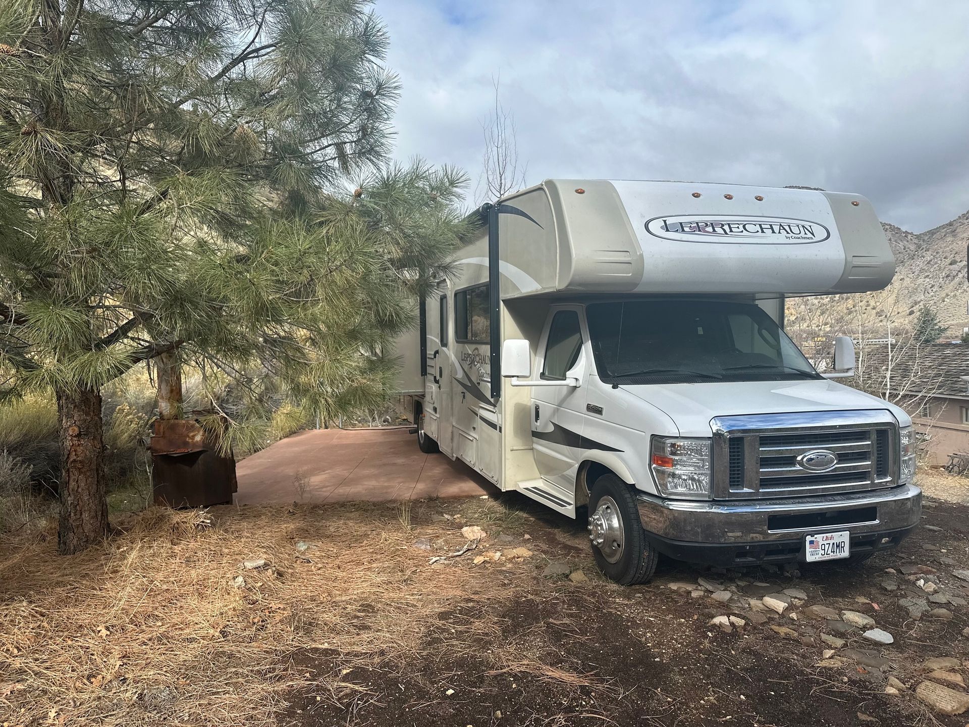 A white rv is parked in a dirt lot next to a tree.