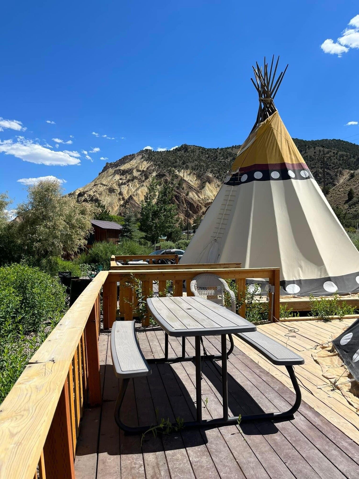 A teepee is sitting on top of a wooden deck next to a picnic table.