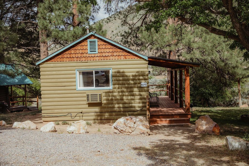 A small log cabin with a porch in the middle of a forest.