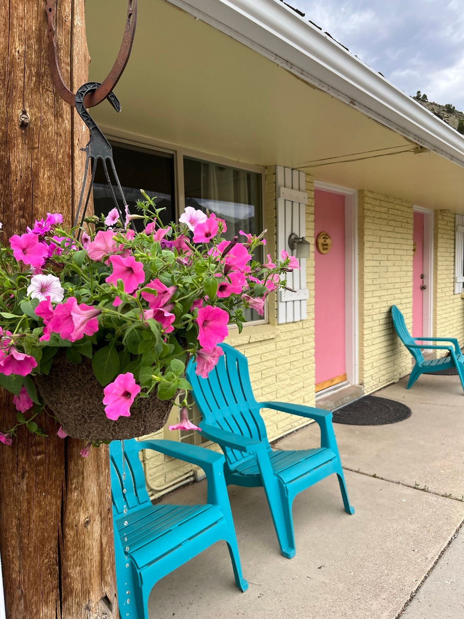 Two blue chairs are sitting in front of a yellow building with pink doors.