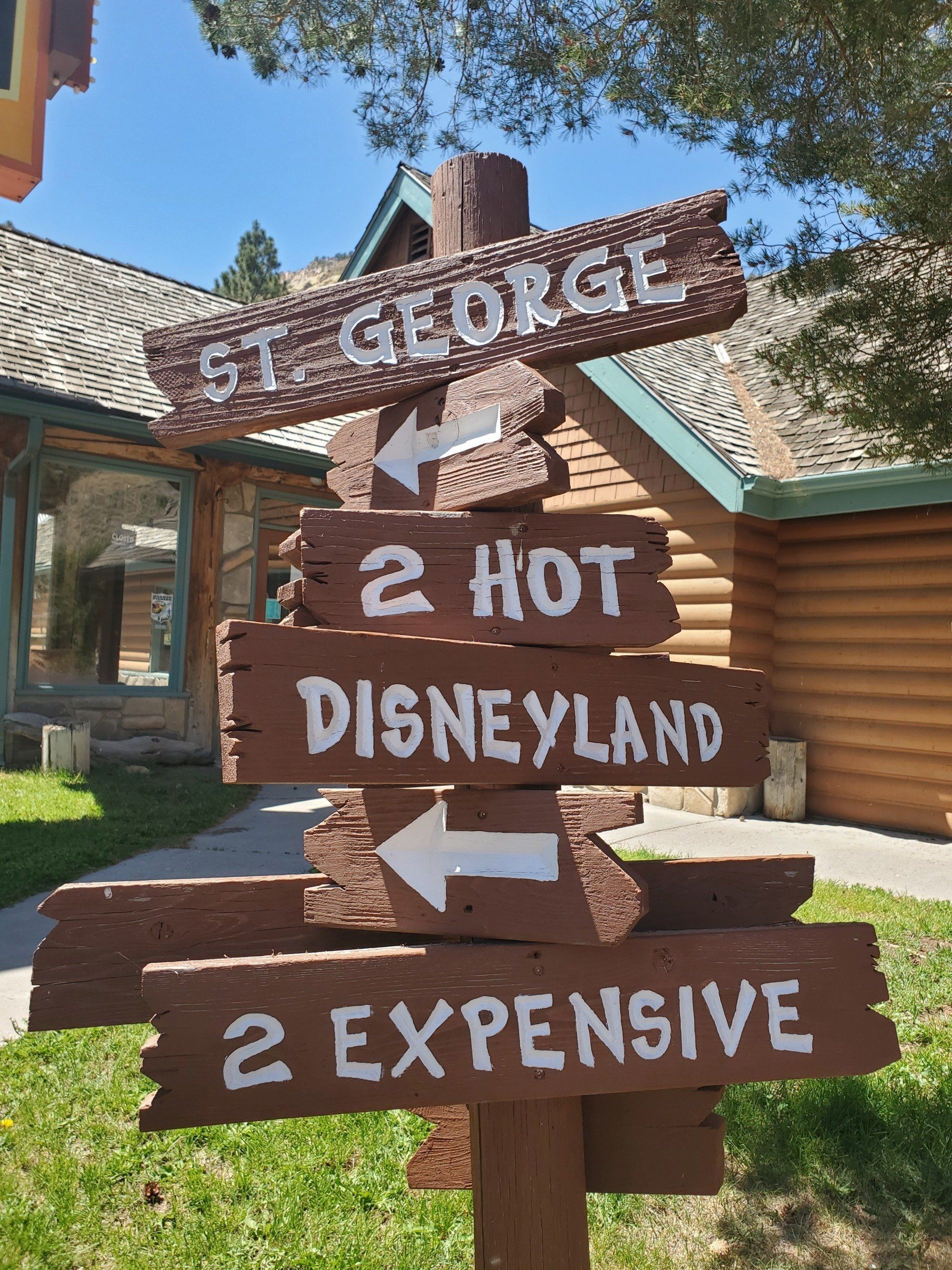 A wooden sign points to st. george 2 hot disneyland and 2 expensive