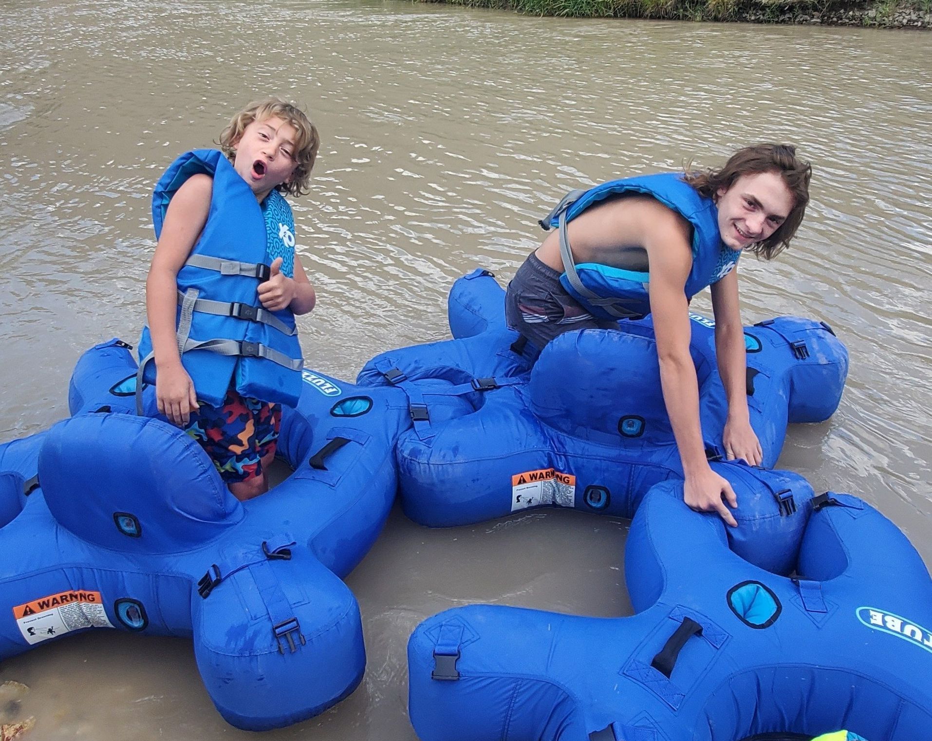 Two young boys are sitting on blue rafts in the water.