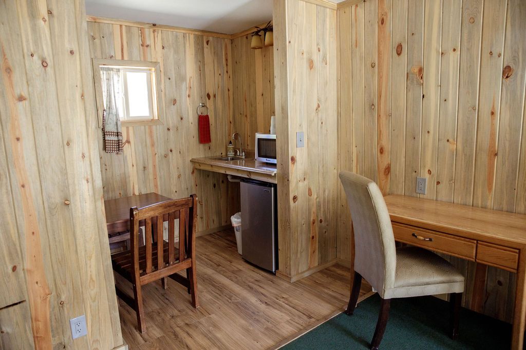 A room with wooden walls , a desk , chairs and a refrigerator.