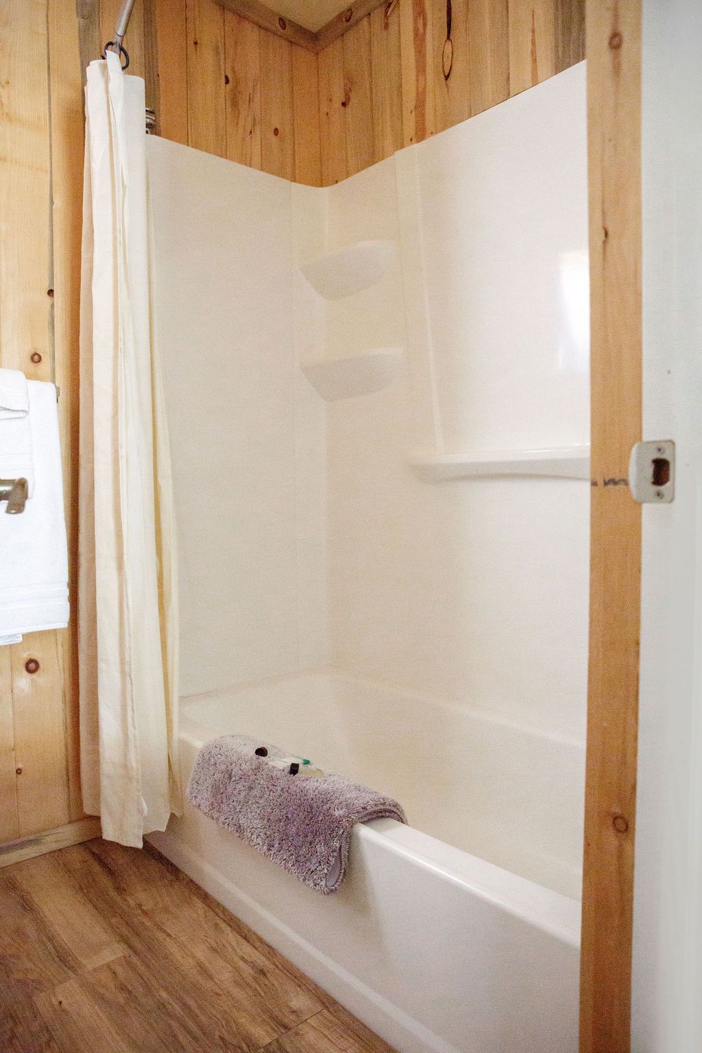 A bathroom with a bathtub , shower , and wooden walls.