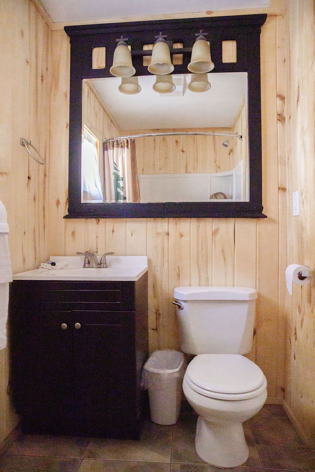 A bathroom with a toilet , sink , mirror and trash can.