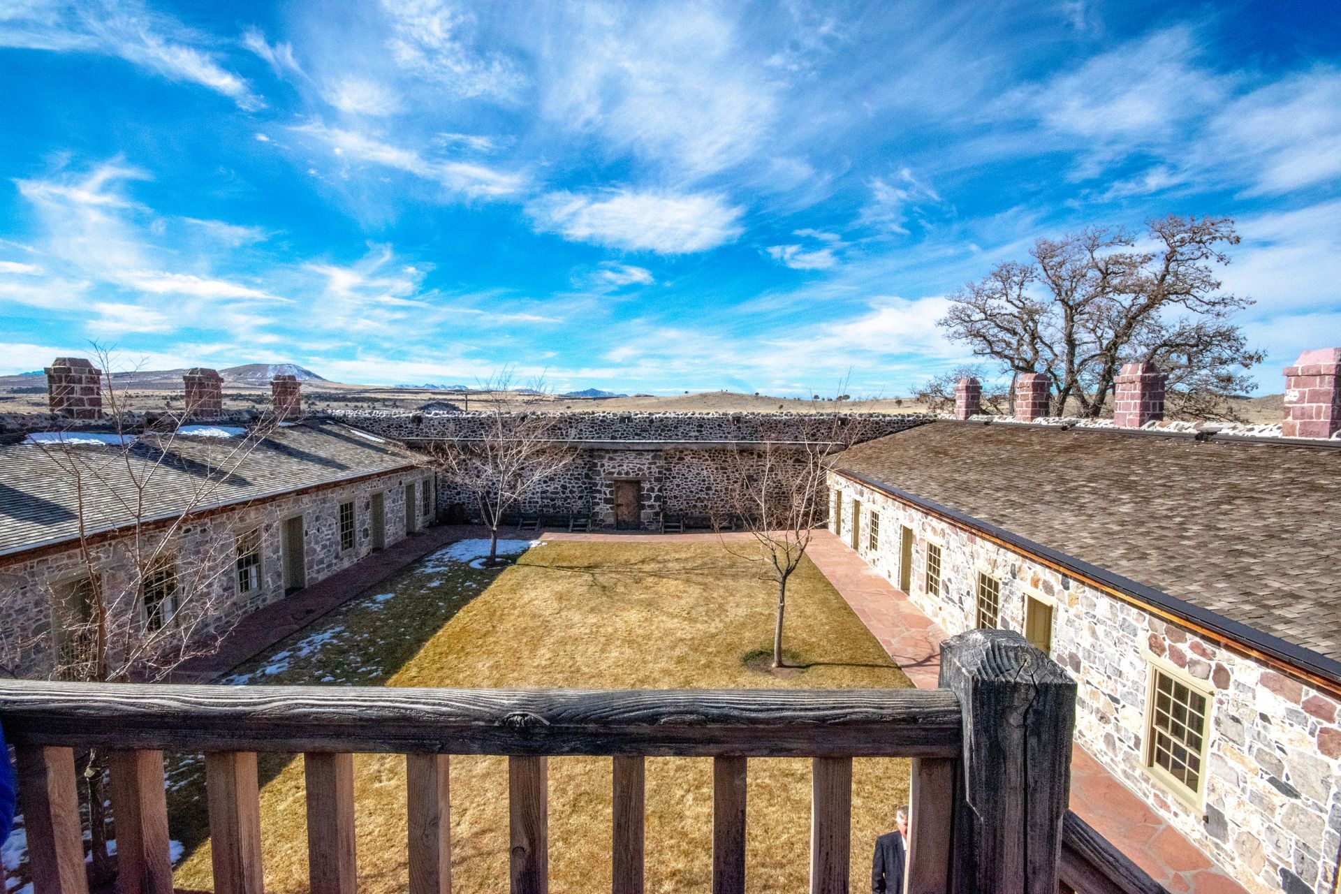 A view of a stone building from a balcony with a wooden railing.