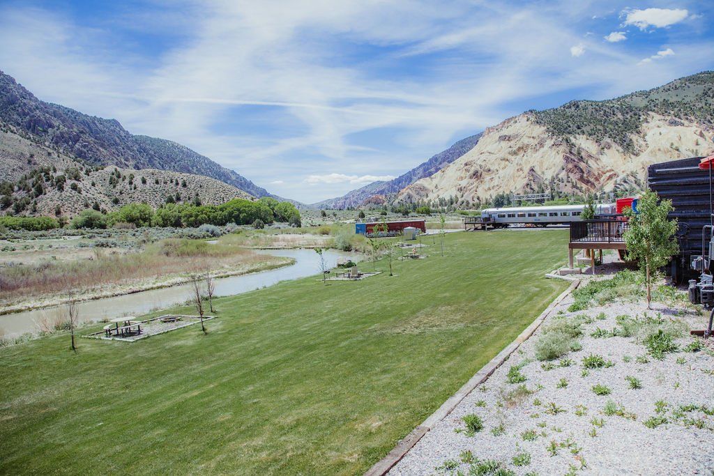 A train is going down the tracks next to a river with mountains in the background.