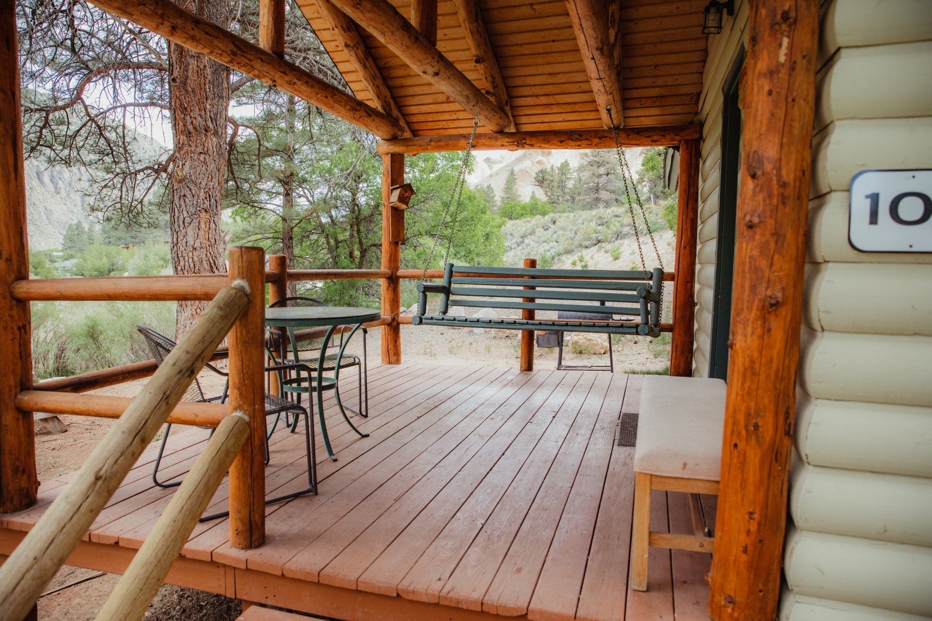 A wooden porch with a bench and a table in front of a log cabin.