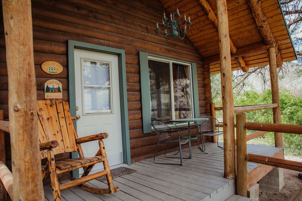 There is a rocking chair on the porch of a log cabin.