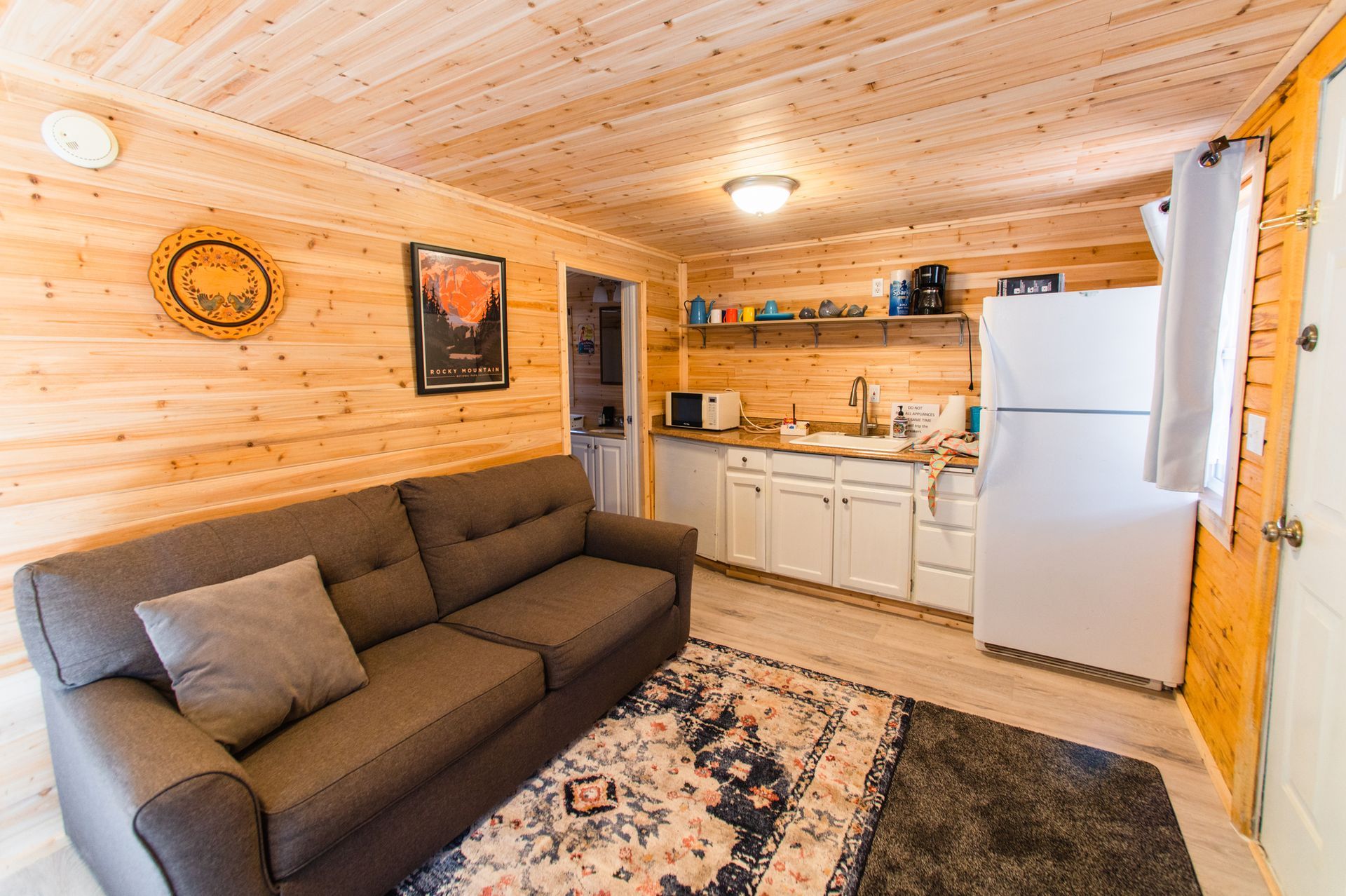 A living room with a couch , rug , refrigerator and kitchen.