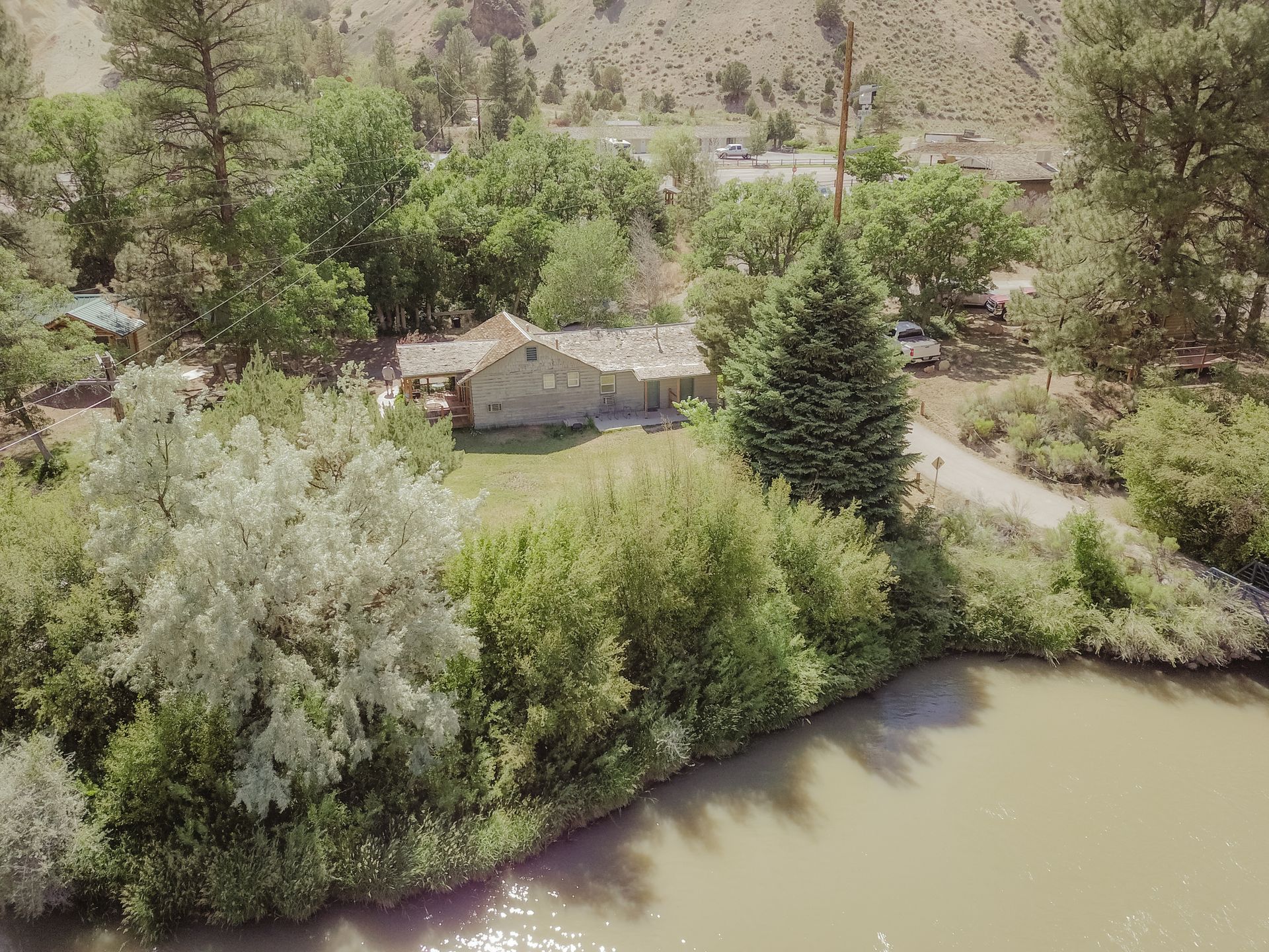 An aerial view of a house on the shore of a river surrounded by trees.