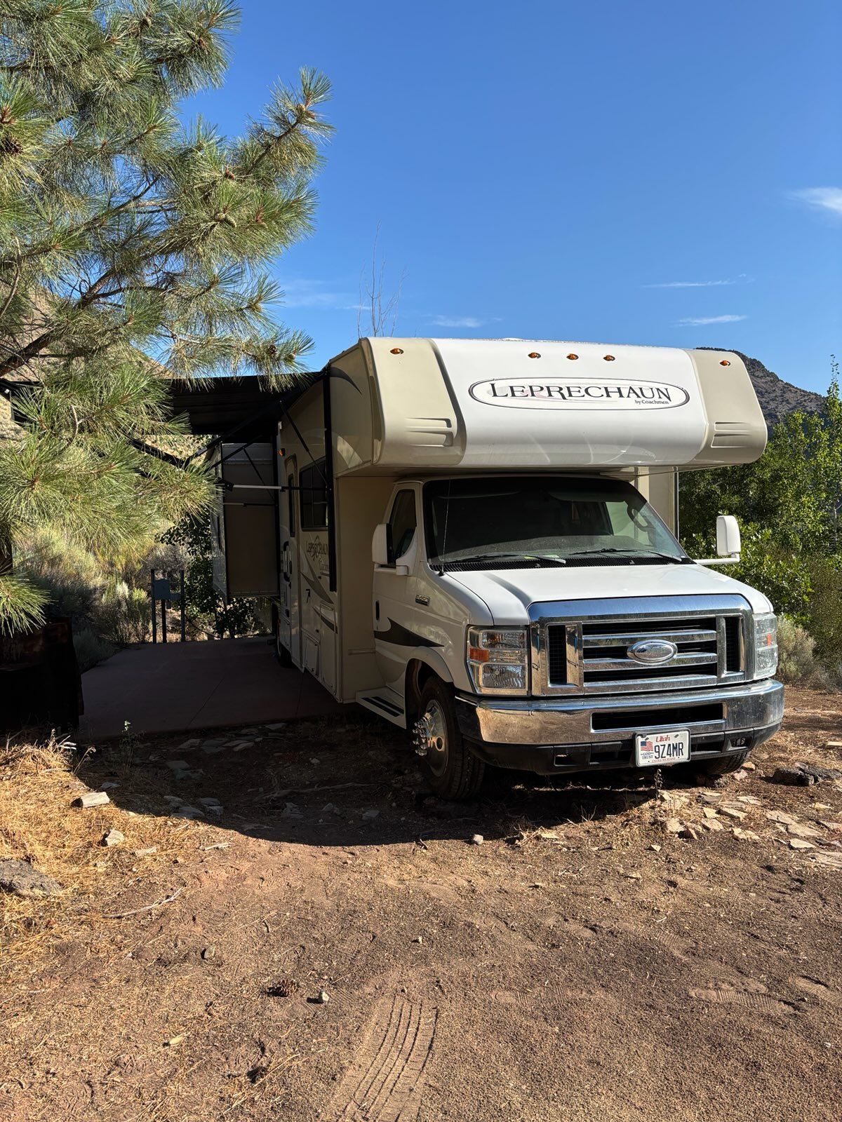 A white rv is parked in a dirt lot next to a tree.