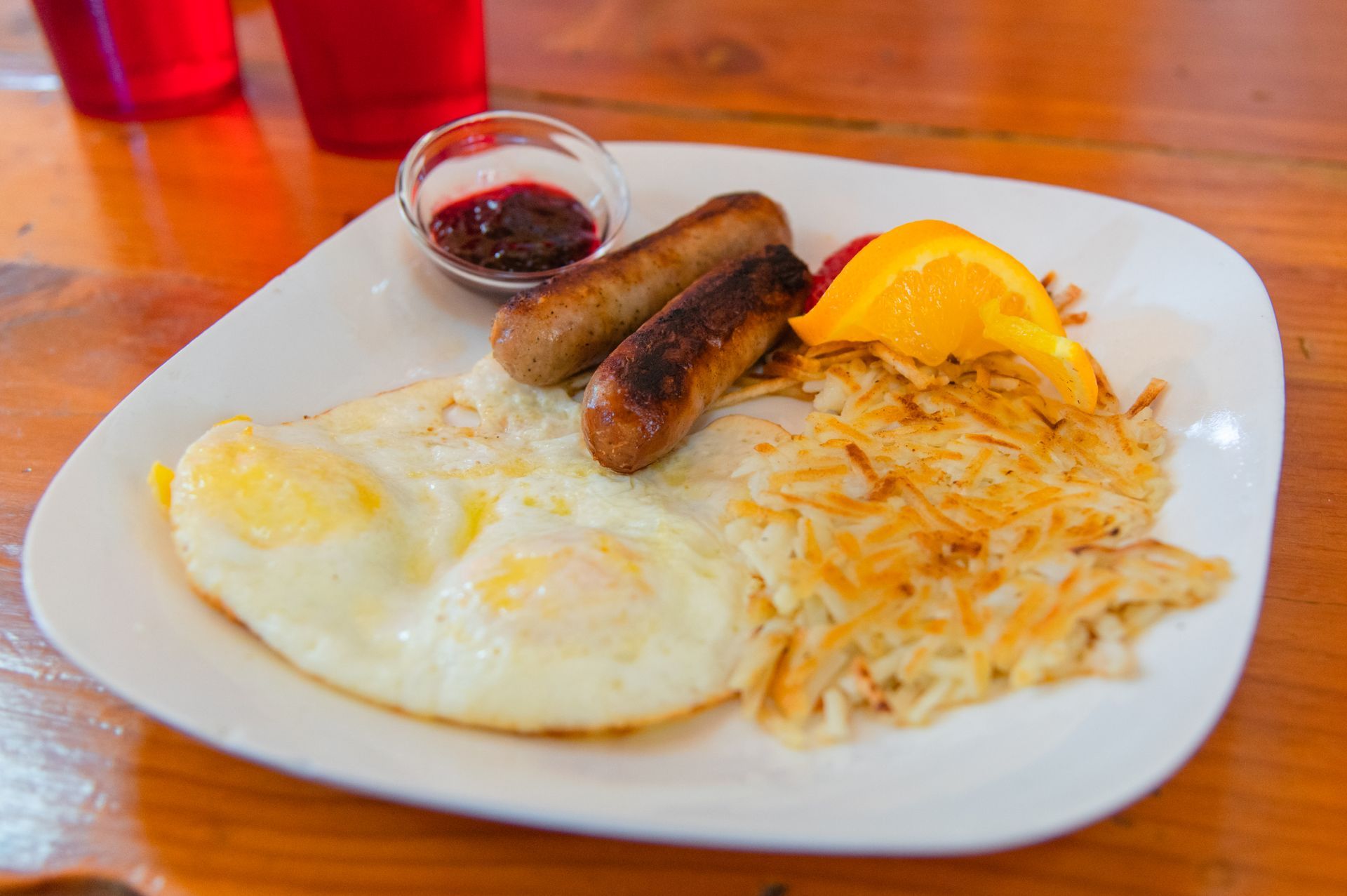 A white plate topped with eggs , sausages , hash browns and orange slices.