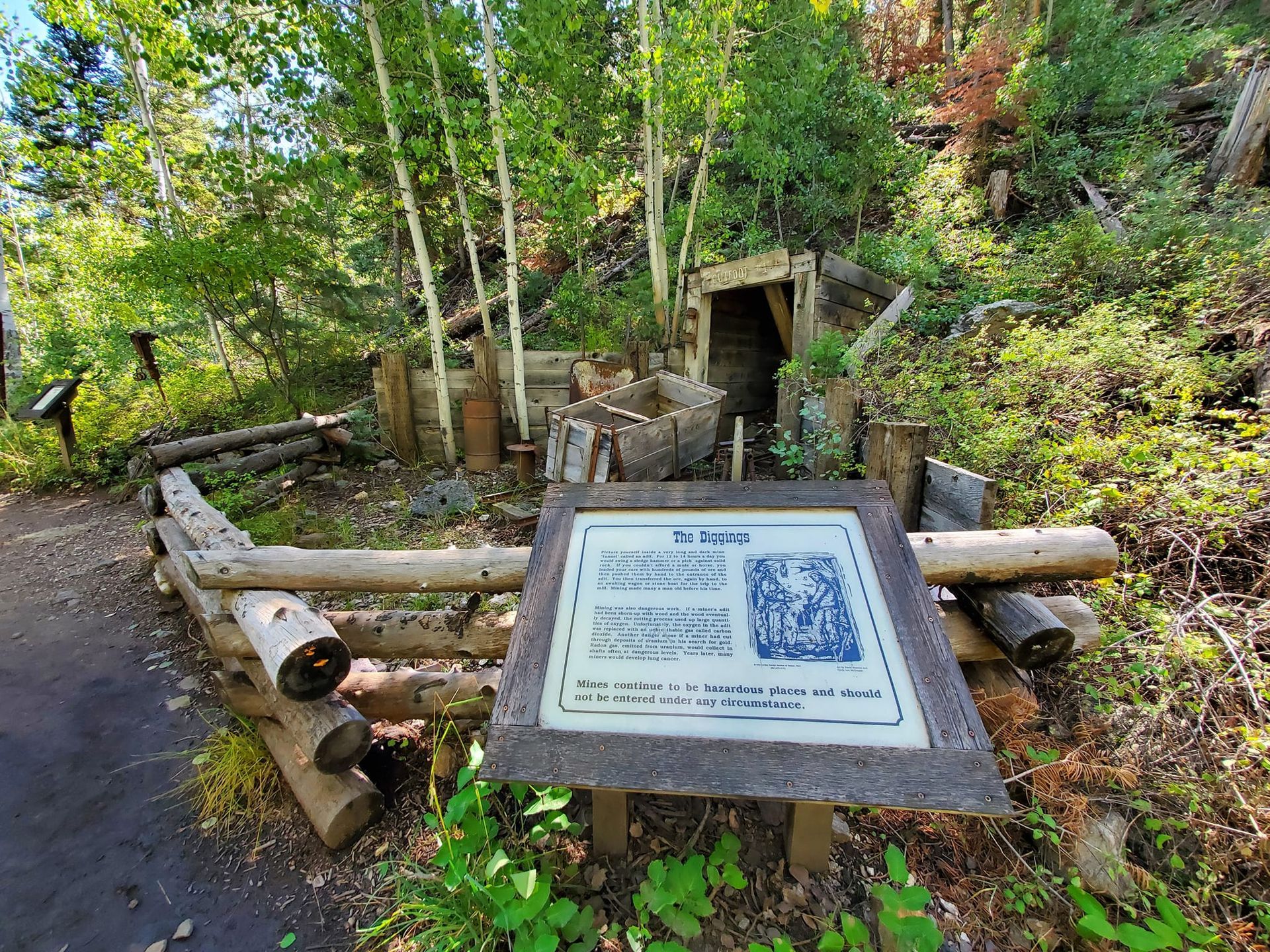 A sign in the middle of a forest next to a wooden fence.