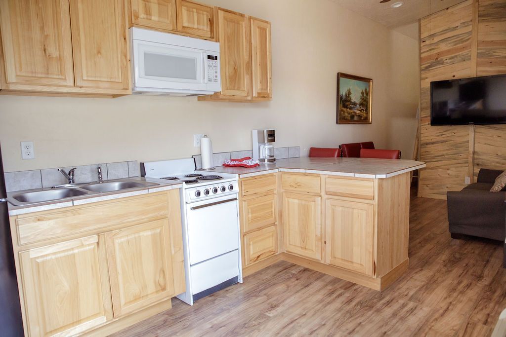 A kitchen with wooden cabinets , a stove , microwave and sink.