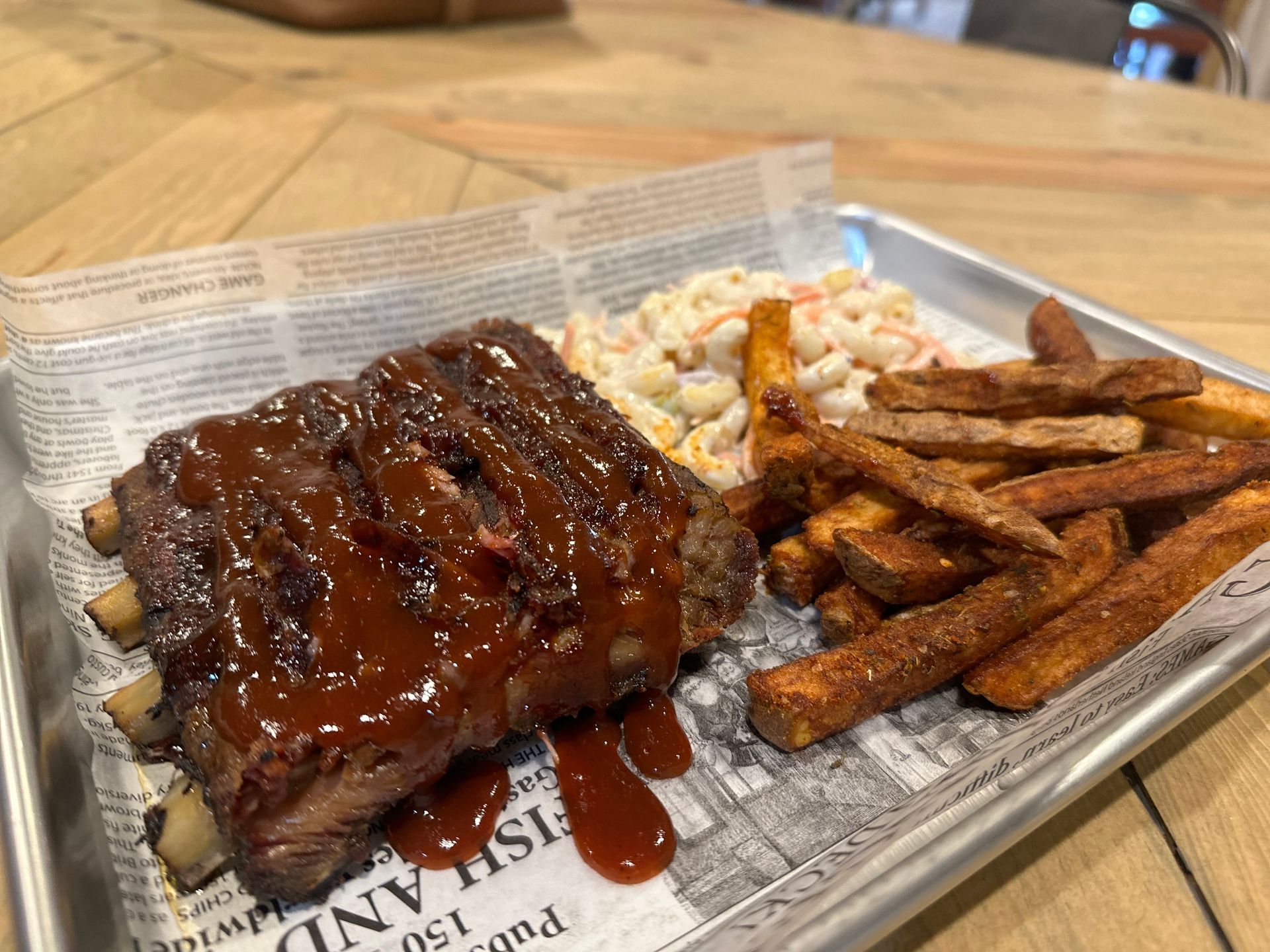 A plate of food with ribs , french fries and coleslaw on a table.