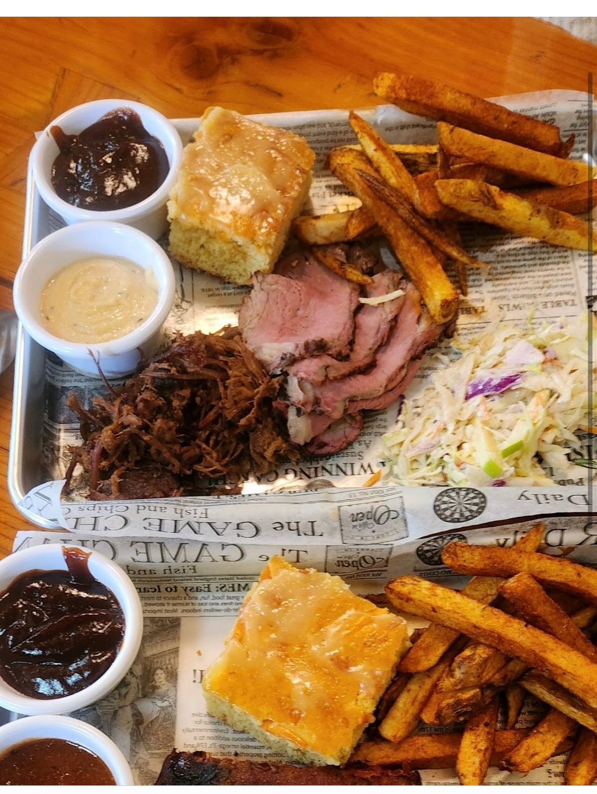 A tray of food with meat , french fries , coleslaw and biscuits on a table.