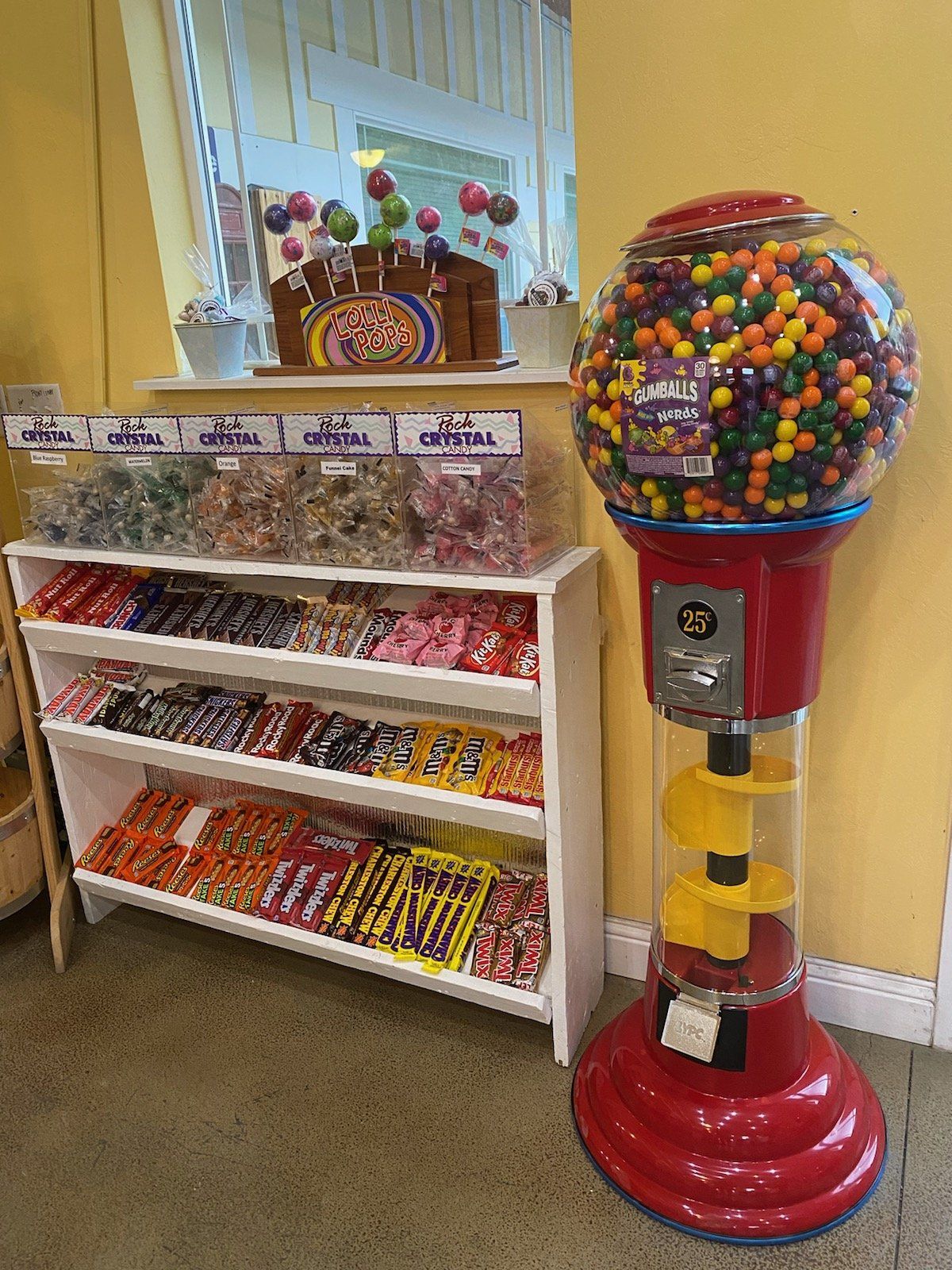 A gumball machine is sitting next to a shelf filled with candy.