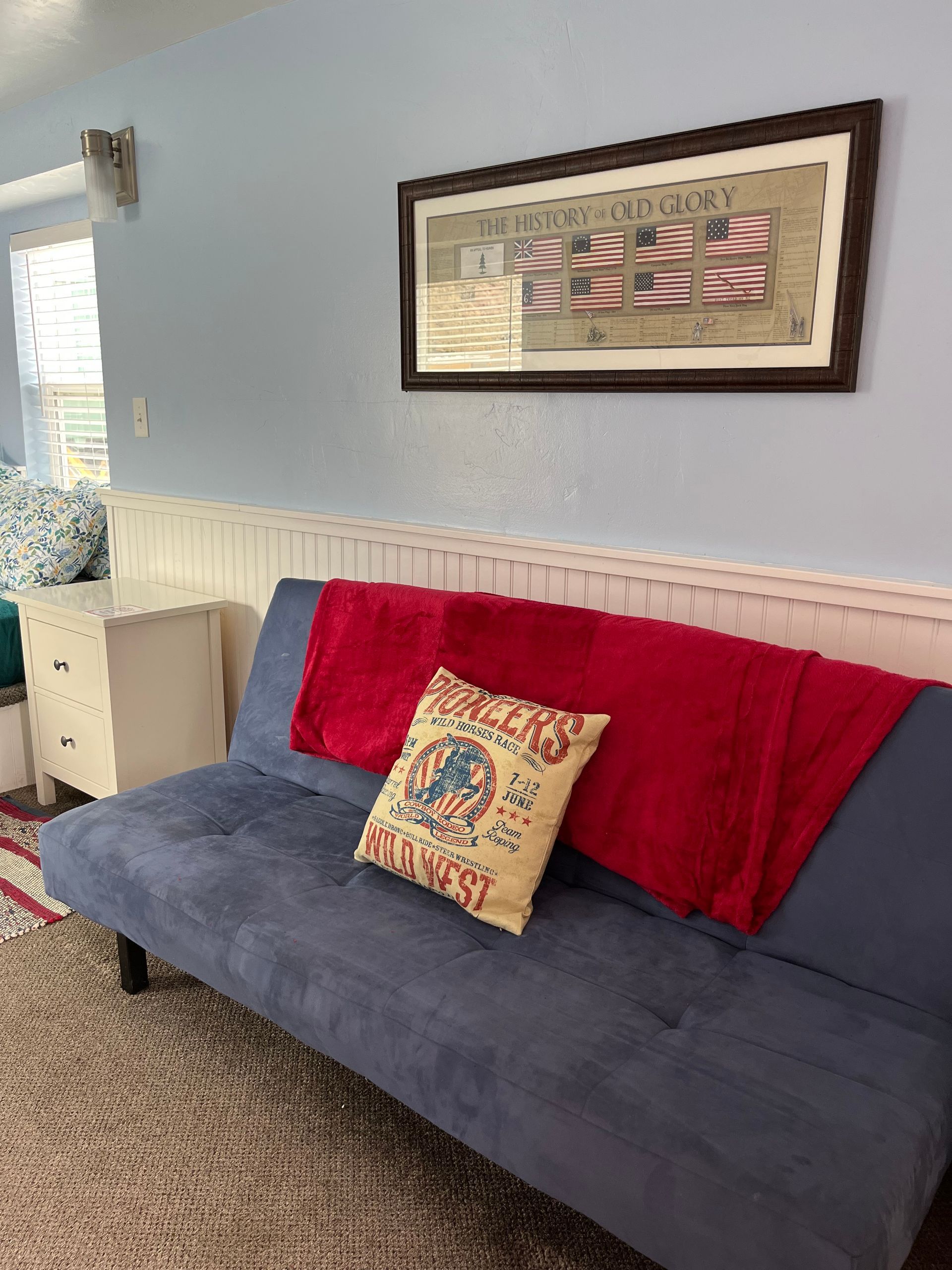 A blue couch with a red blanket and a yellow pillow in a living room.