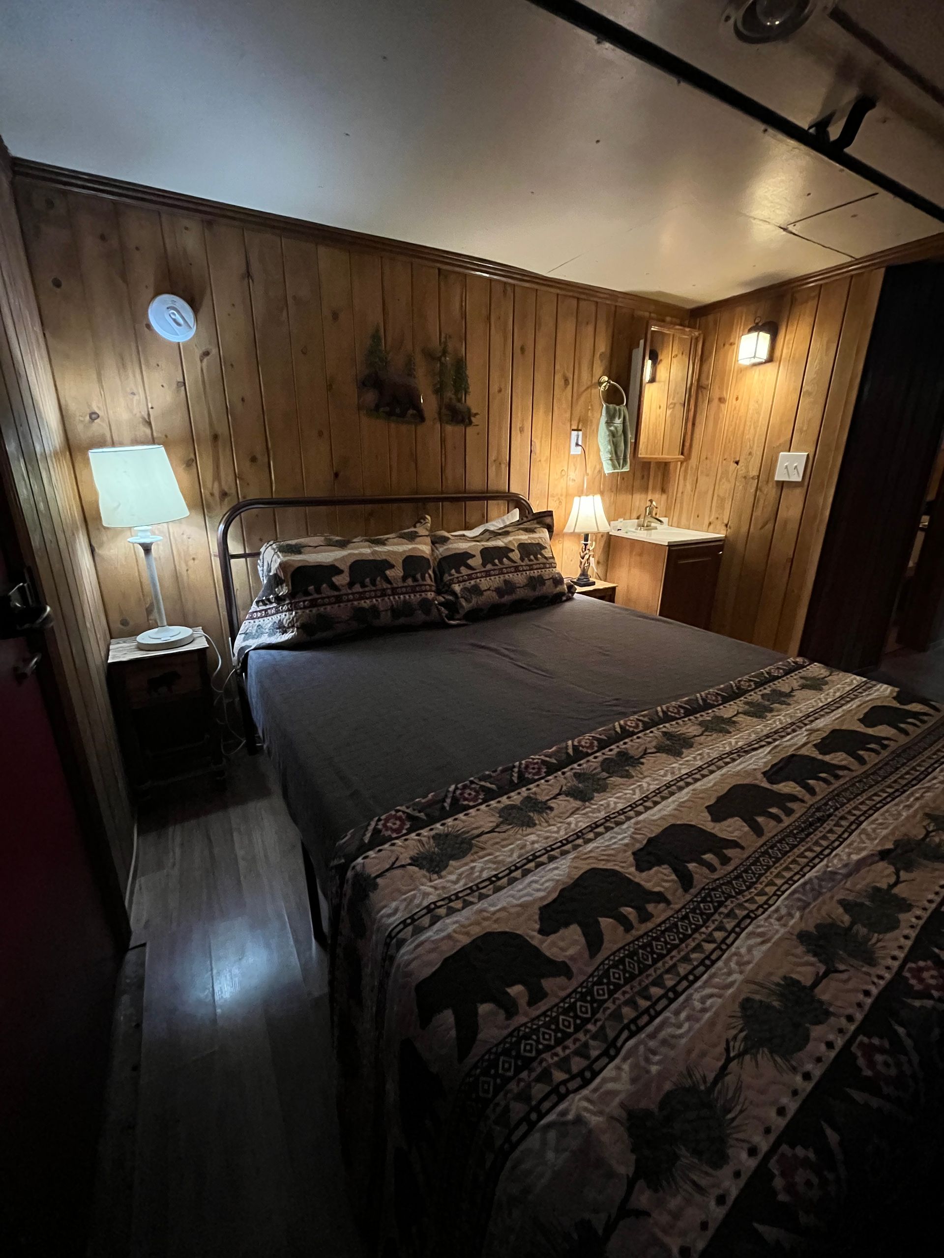 A bedroom with a bed , two lamps , a nightstand , and a wooden wall.