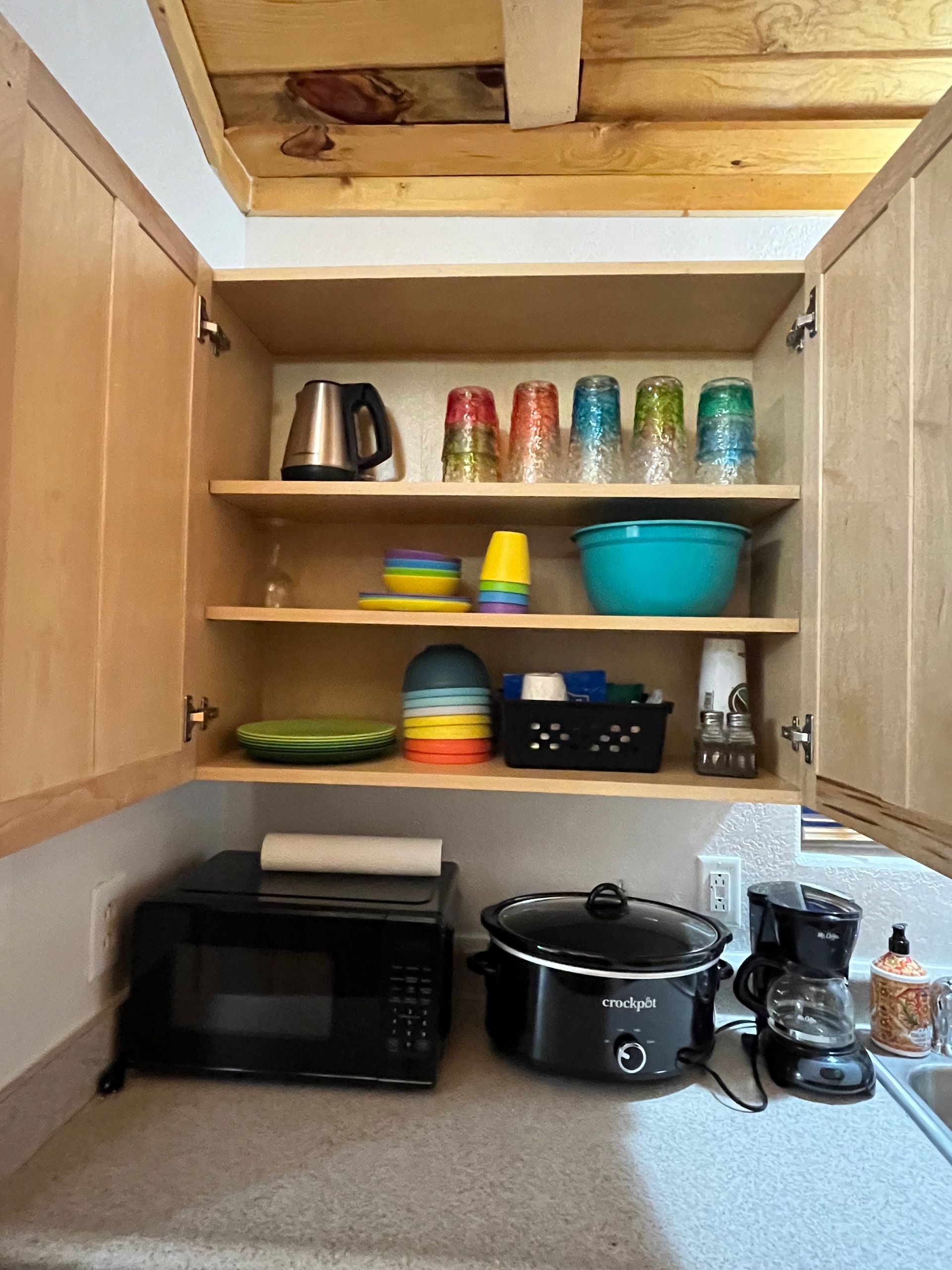 A kitchen with a microwave , pot , bowls , glasses , and a coffee maker.