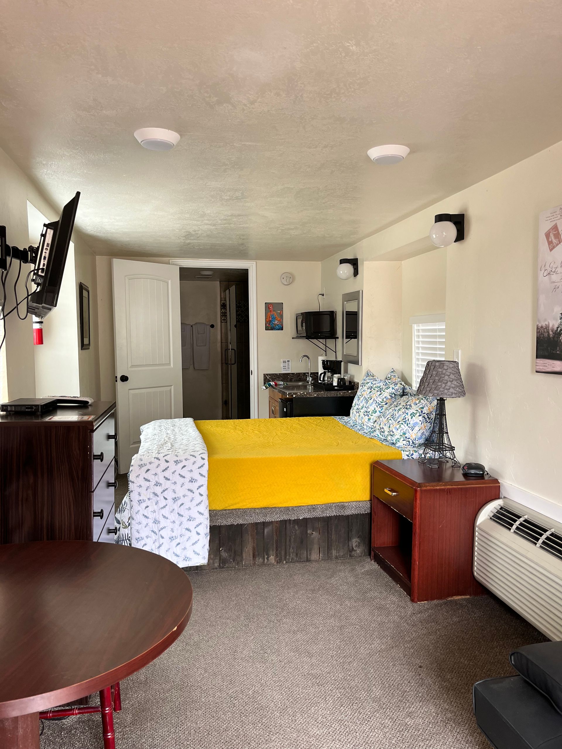 A hotel room with a bed , table , nightstand and television.