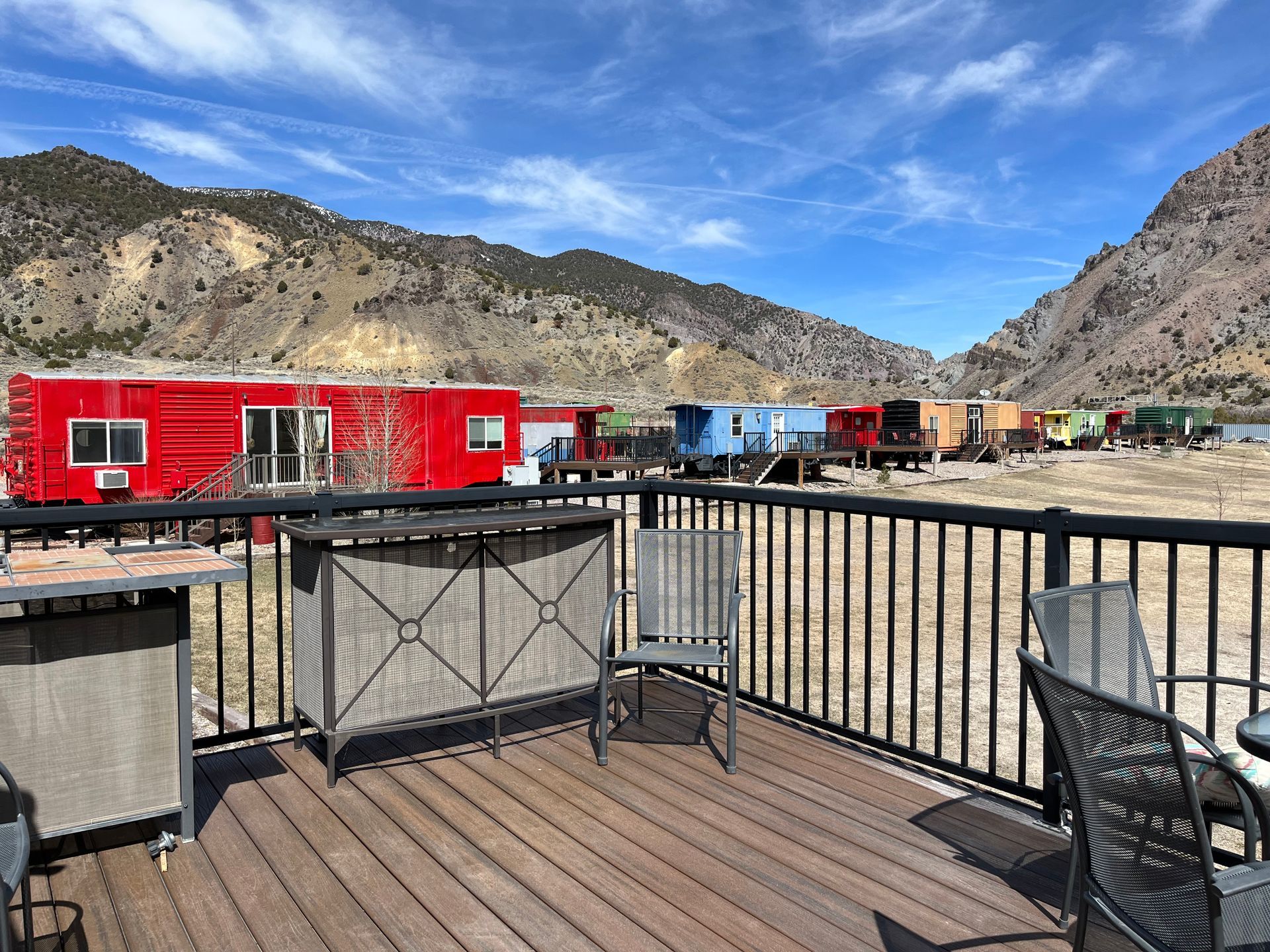 A deck with chairs and a table with a train in the background.