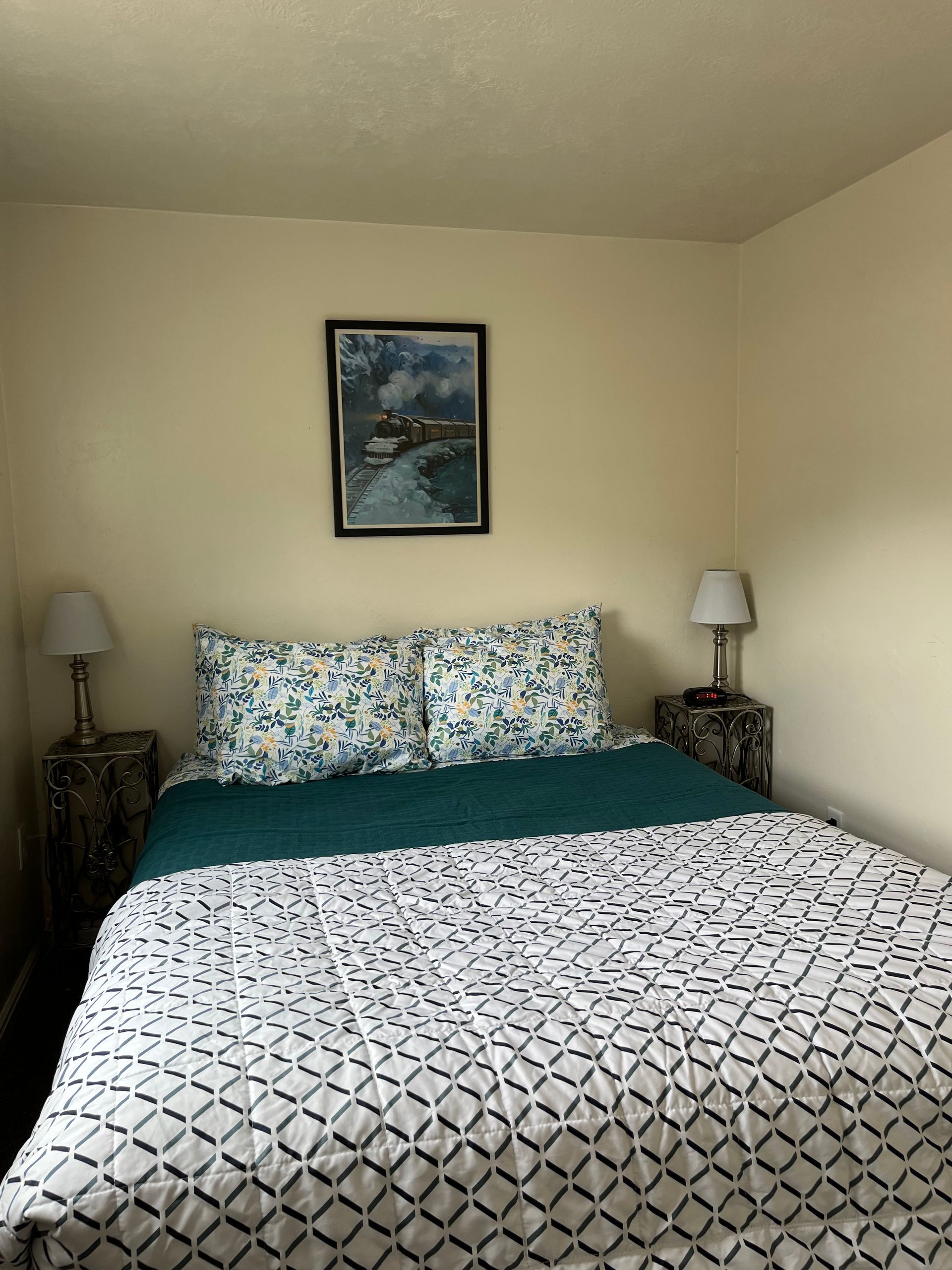 A bedroom with a bed , two lamps and a painting on the wall.