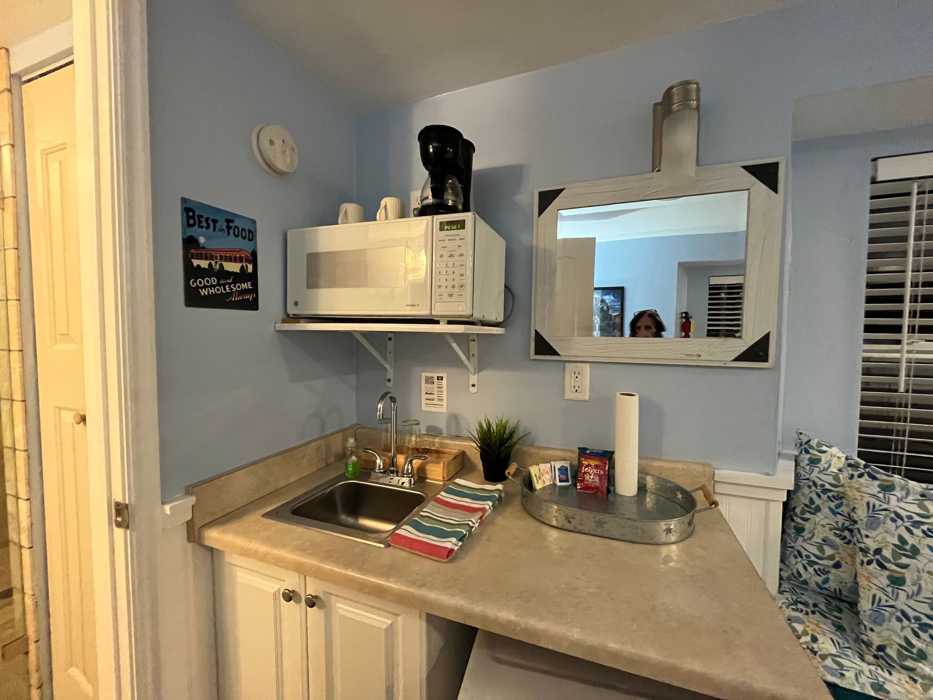 A kitchen with a sink , microwave , and mirror