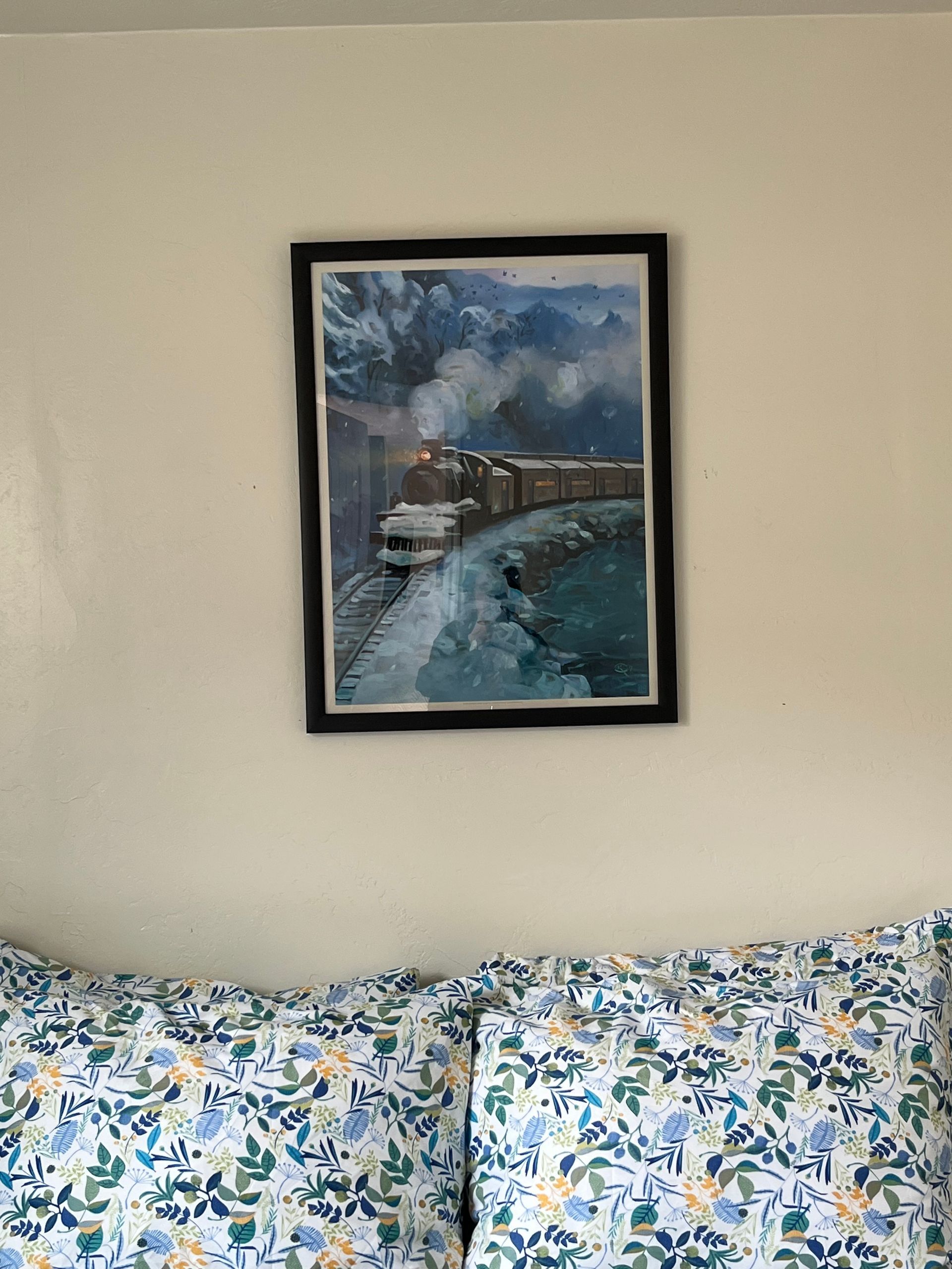 A painting of a train is hanging on a wall next to a bed.