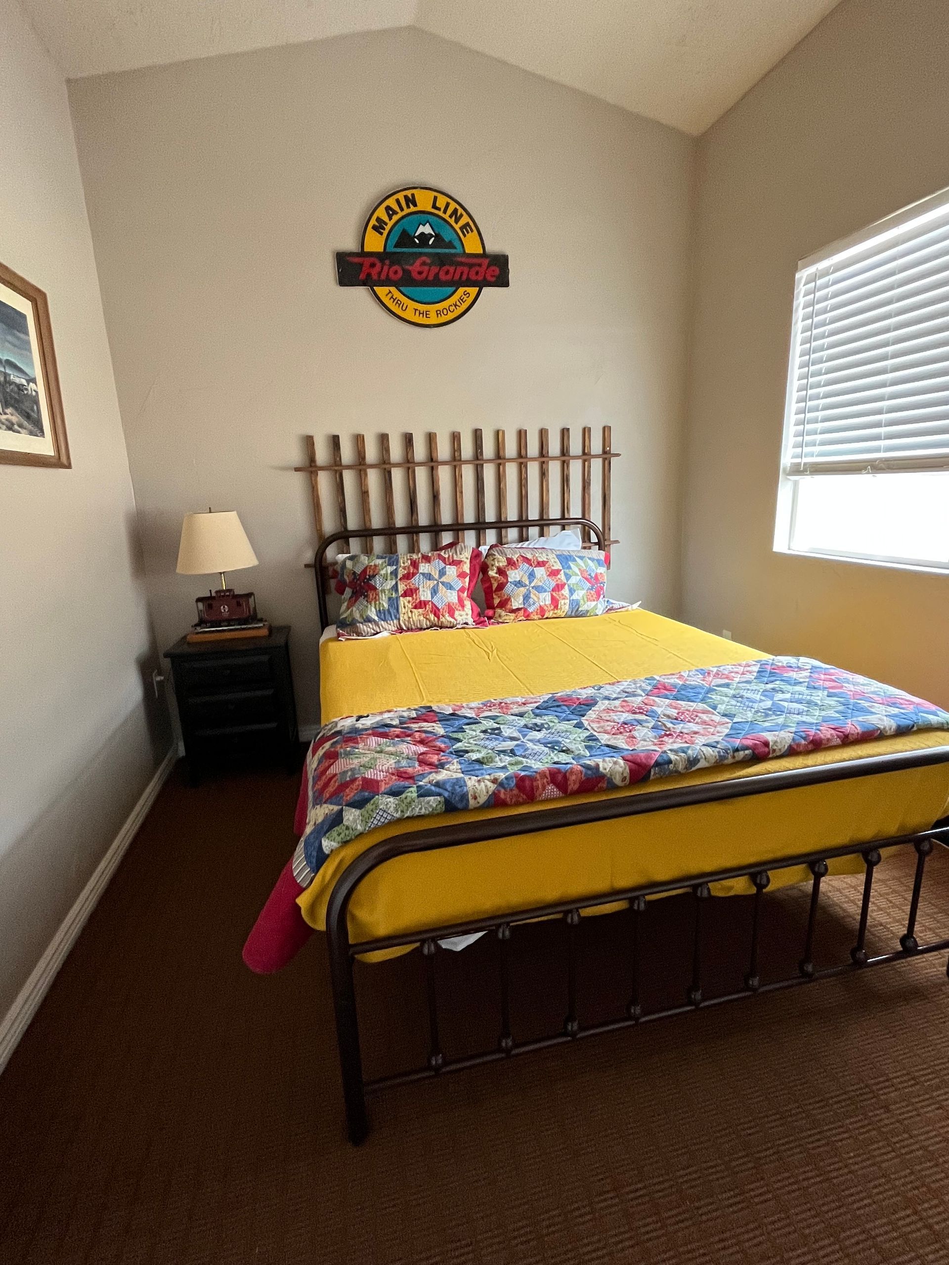 A bedroom with a bed , nightstand , lamp and a sign on the wall.