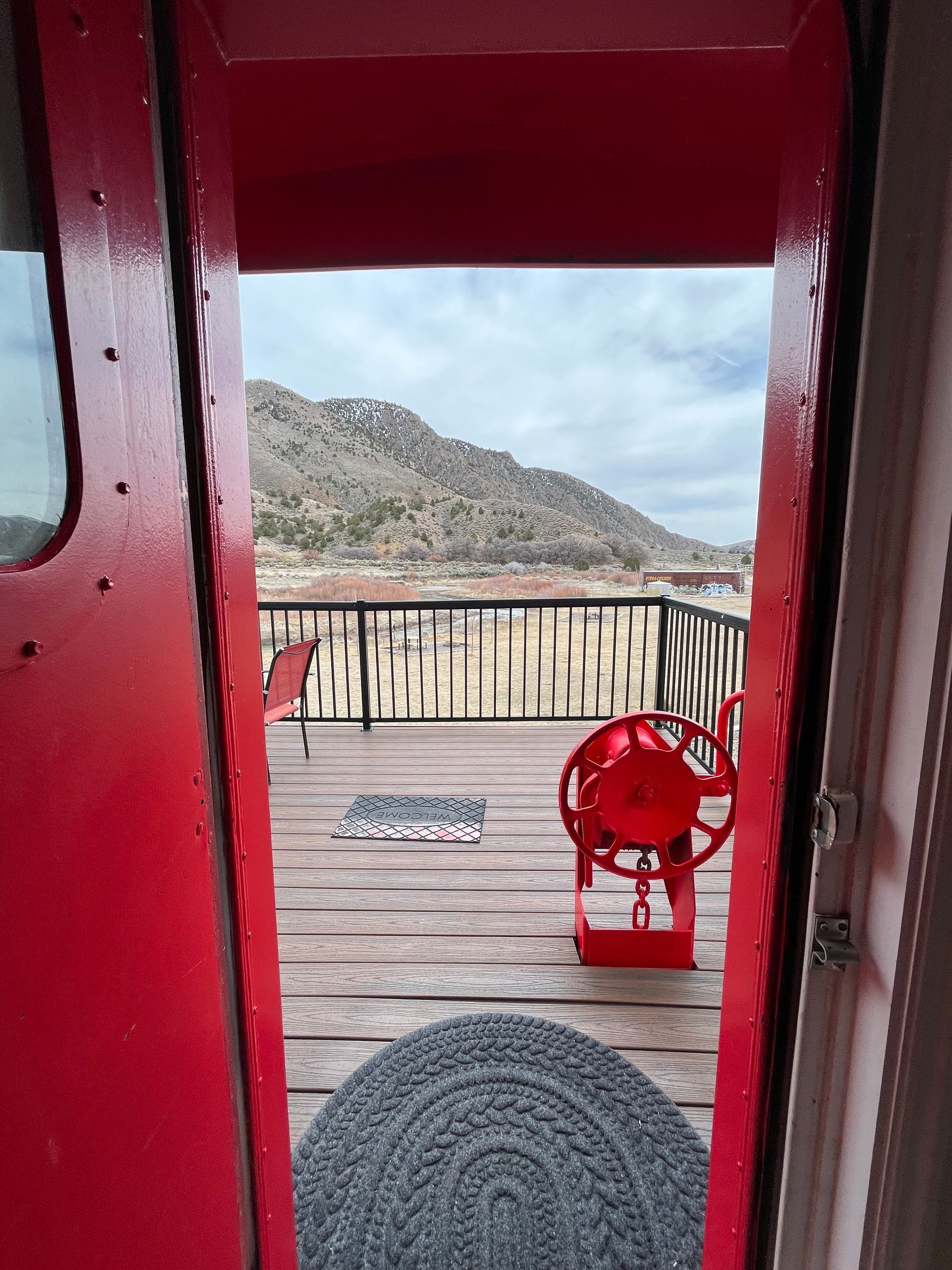 A red door is open to a deck with a ferris wheel and mountains in the background.