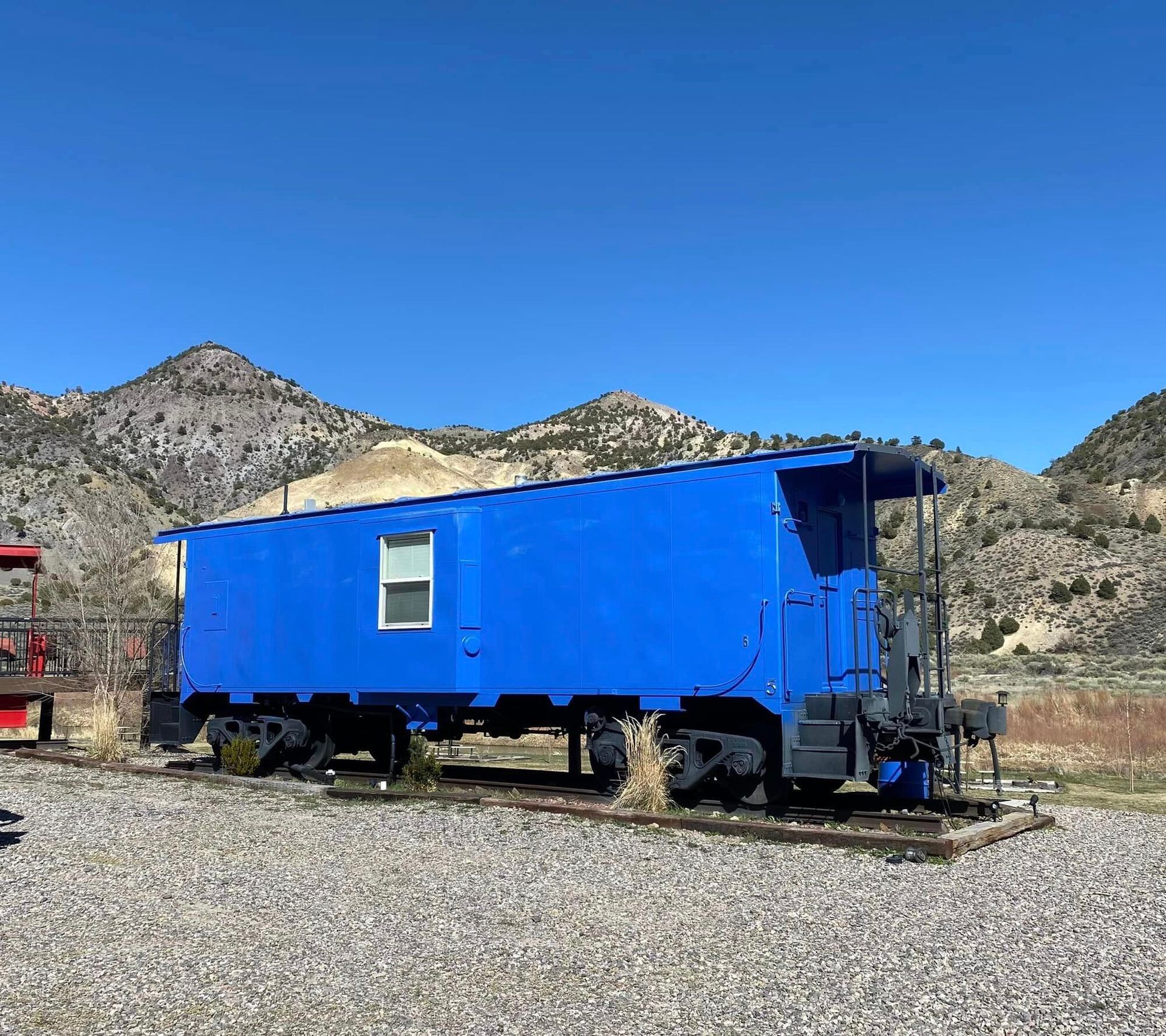 A blue train car with a window and mountains in the background