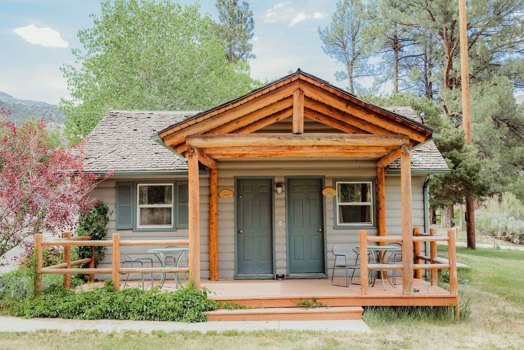 A small house with a porch and trees in the background.