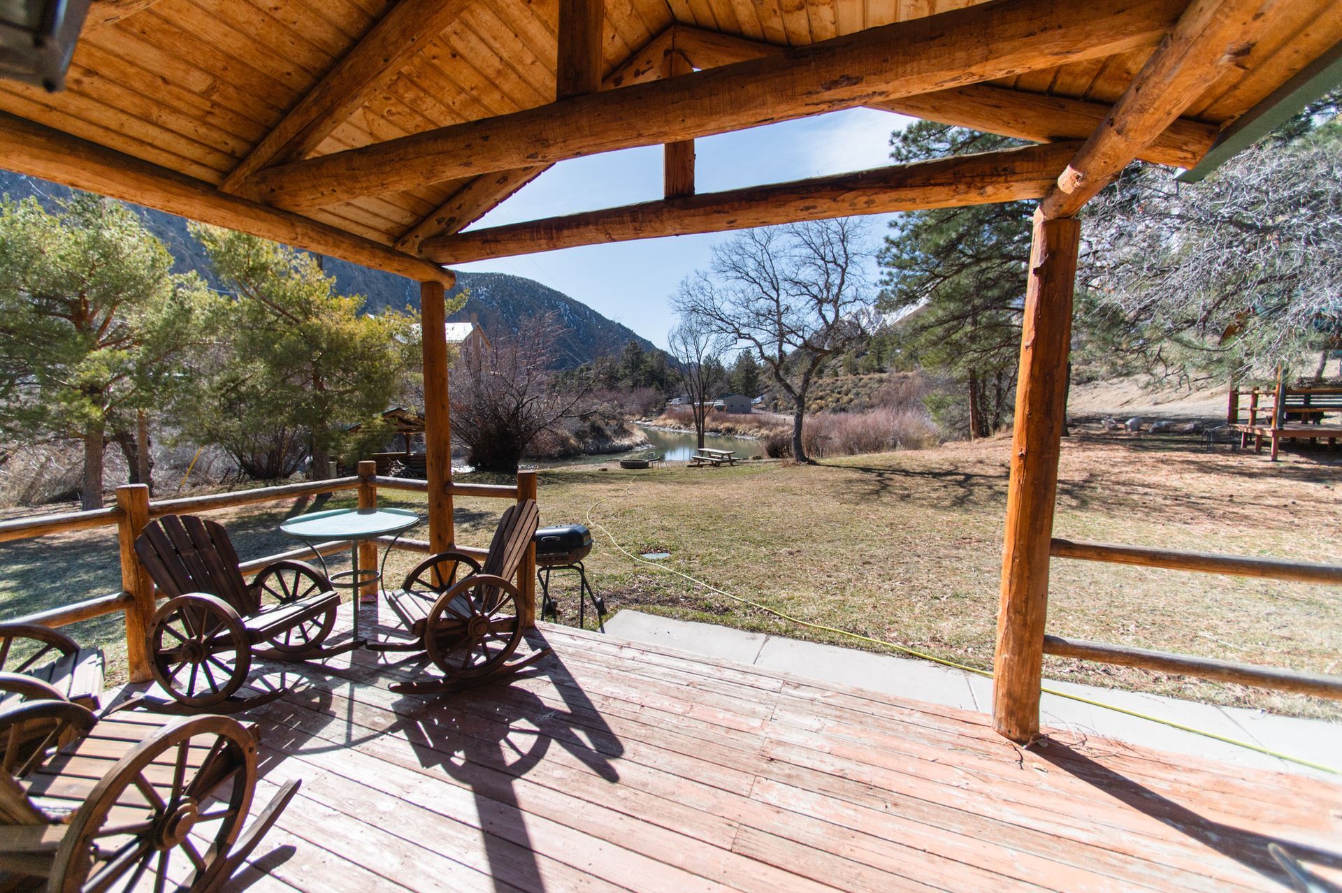 A wooden deck with rocking chairs and a table under a wooden roof.