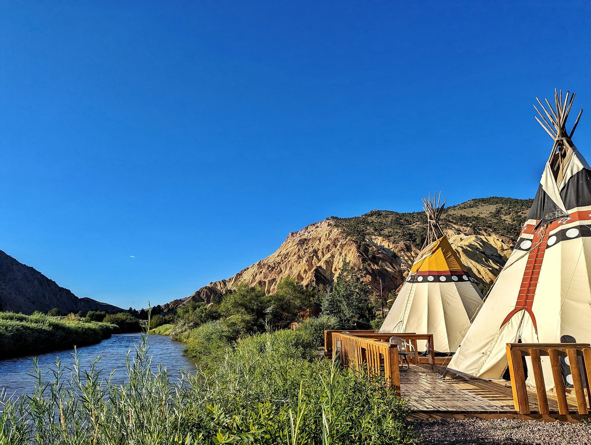 a couple of teepees sitting next to a river with mountains in the background .