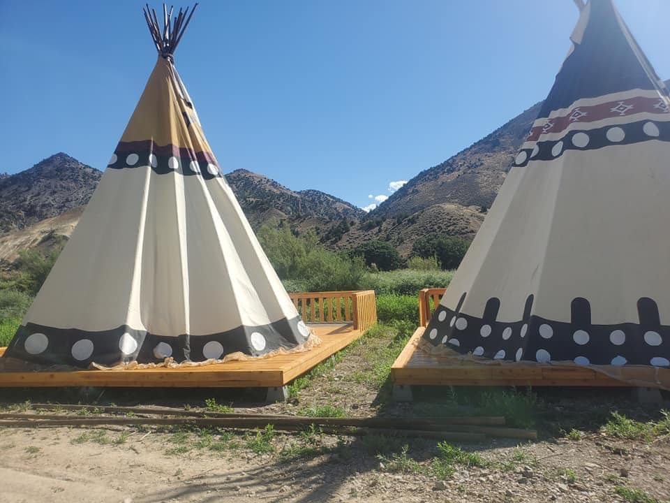 Two teepees are sitting next to each other with mountains in the background