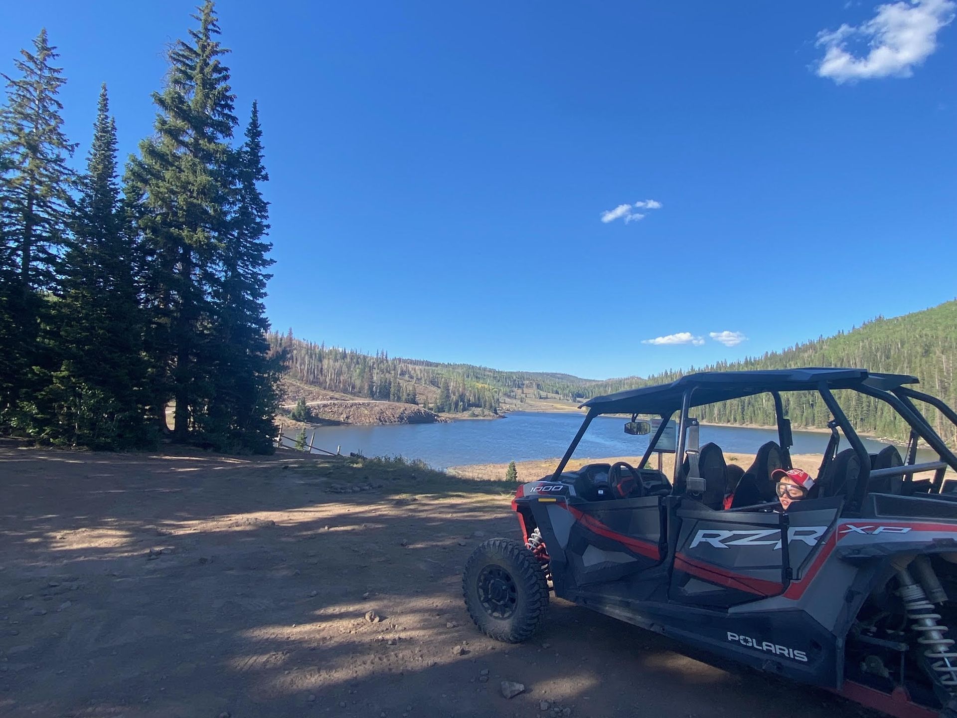 A four person atv is parked on a dirt road next to a lake.