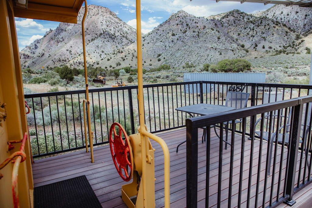 A balcony with a table and chairs and mountains in the background.