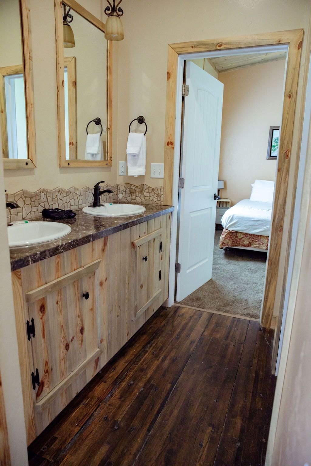 A bathroom with two sinks and two mirrors leading to a bedroom.