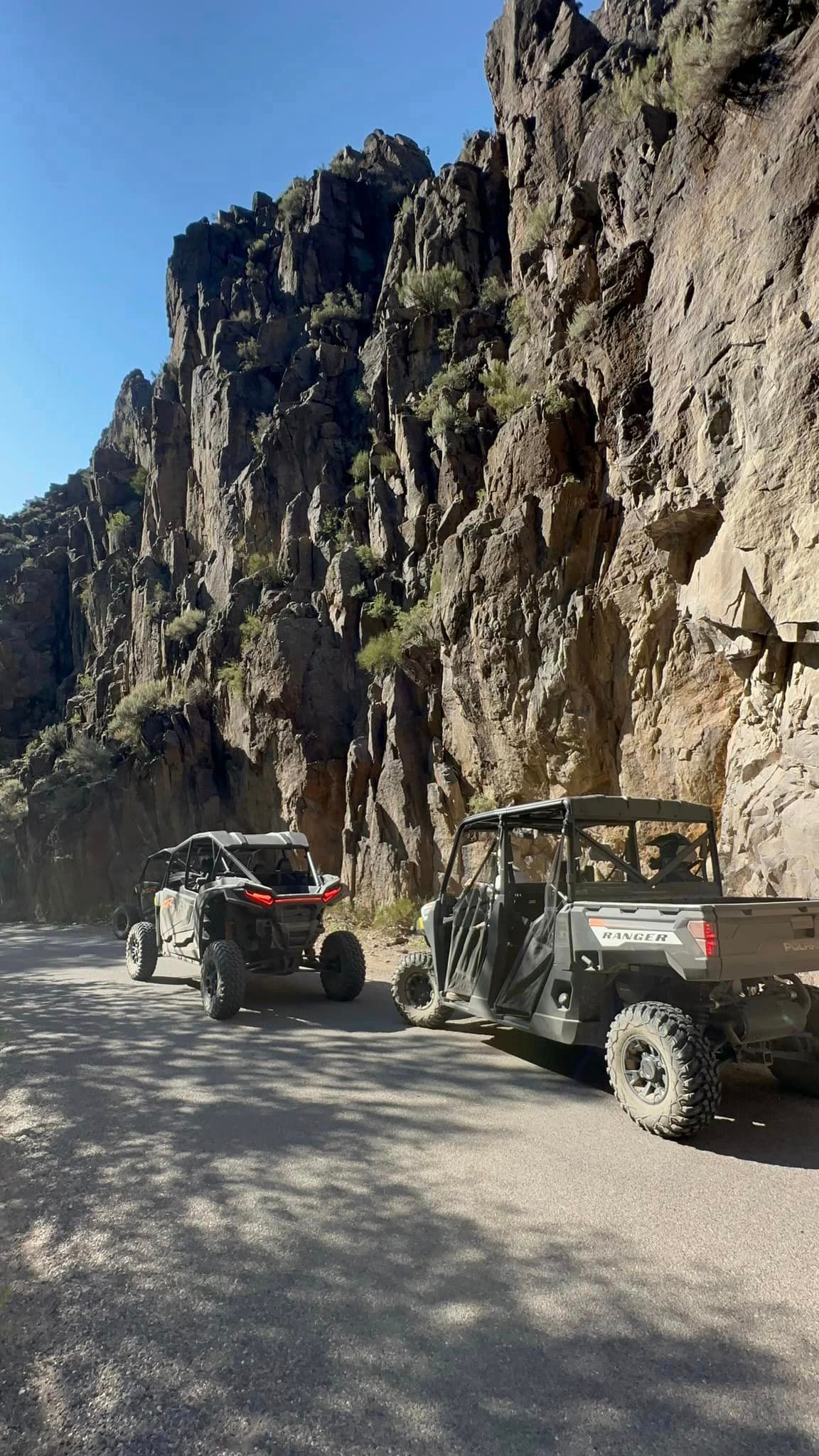 Two atvs are parked on the side of a dirt road next to a mountain.