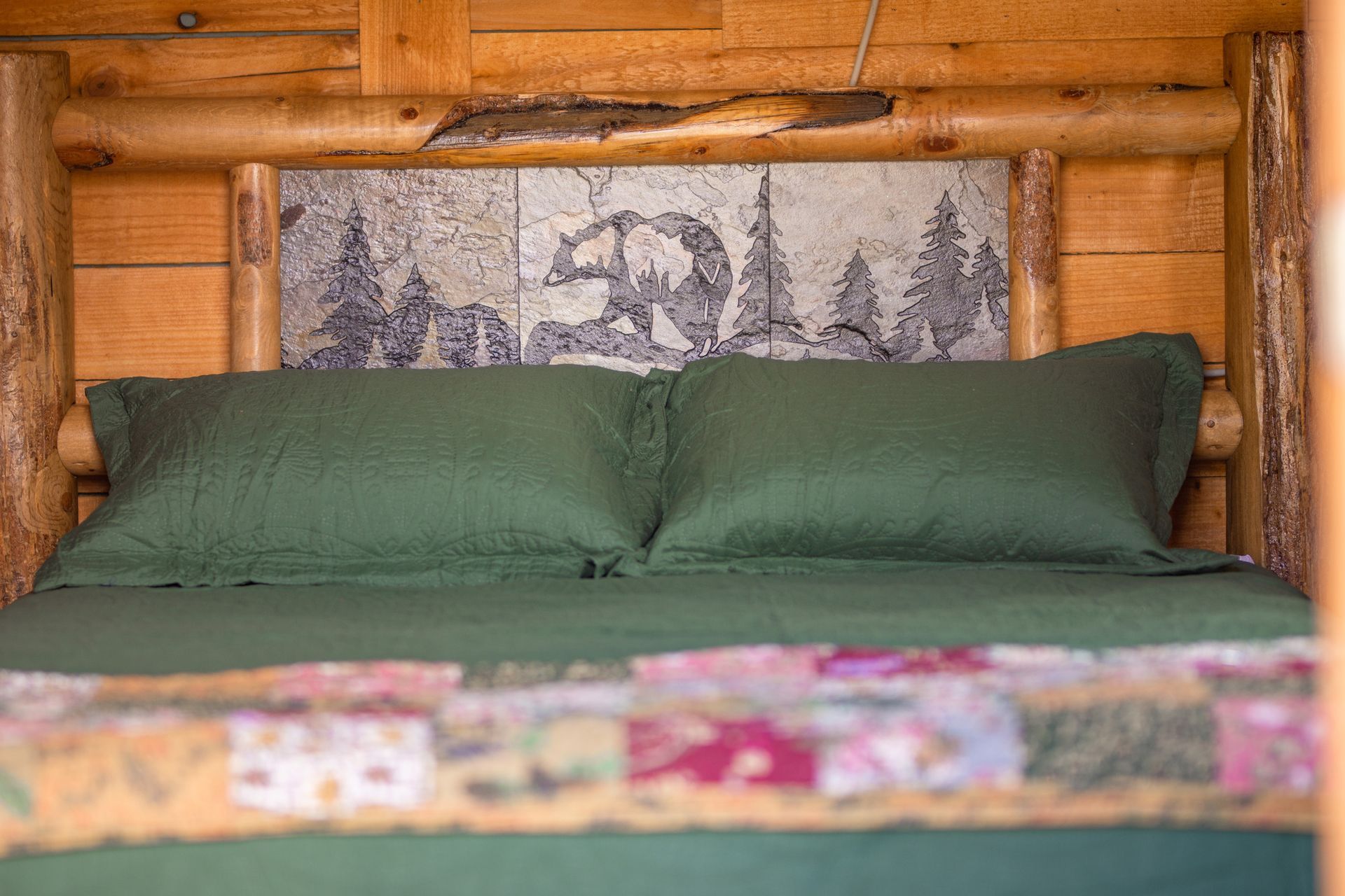 A bed with green sheets and pillows in a log cabin.