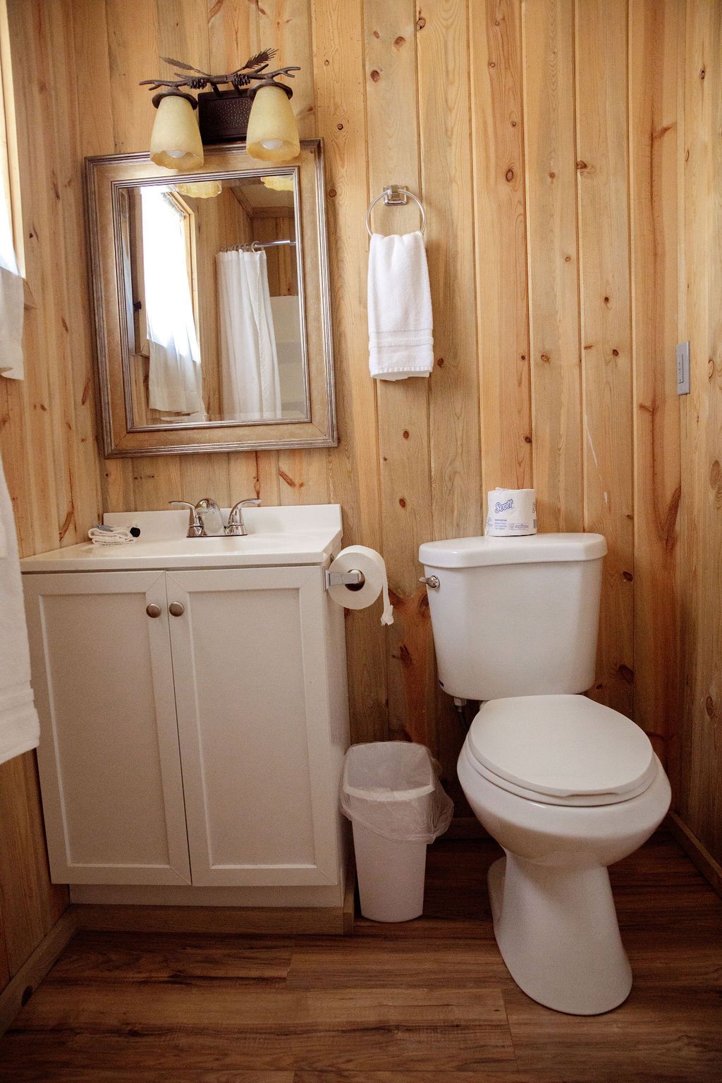 A bathroom with a toilet , sink , mirror and trash can.