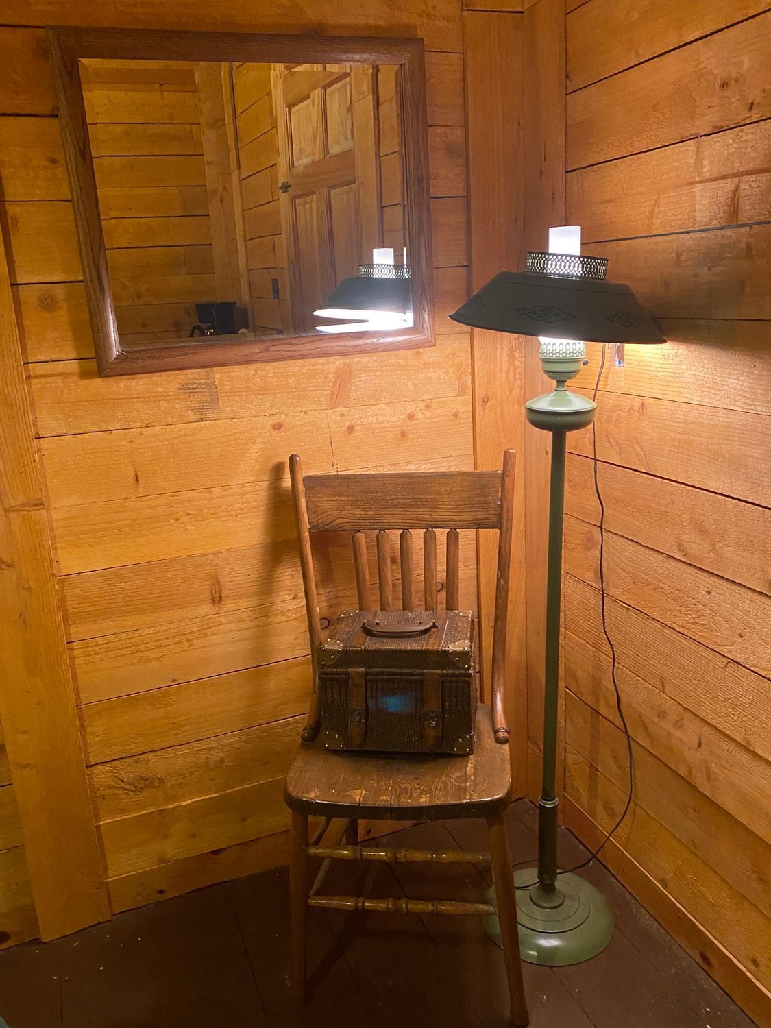 A wooden chair is sitting in a corner of a room next to a lamp and a mirror.