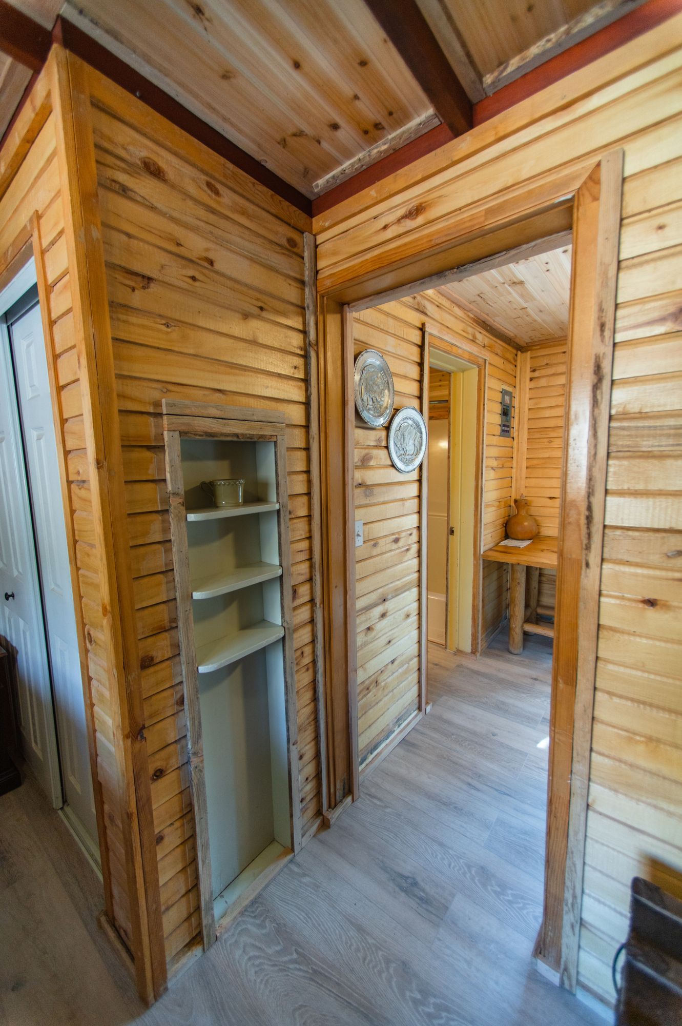 A hallway in a log cabin with wooden walls and a doorway leading to a room.