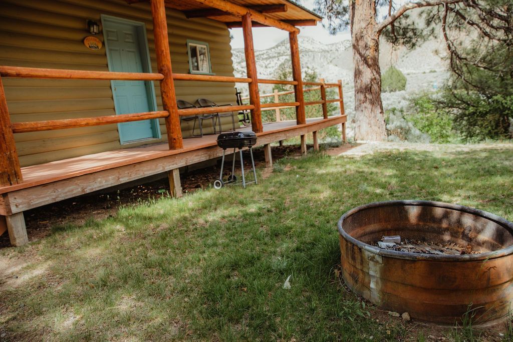 A log cabin with a porch and a fire pit in front of it.