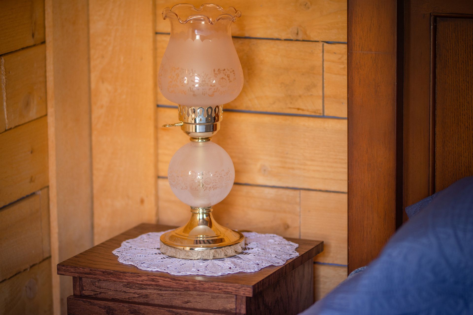 A lamp is sitting on a wooden nightstand next to a bed.