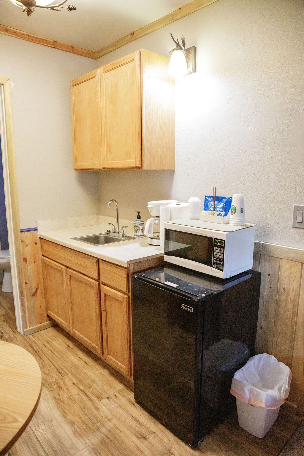 A kitchen with a sink , microwave , refrigerator and trash can.