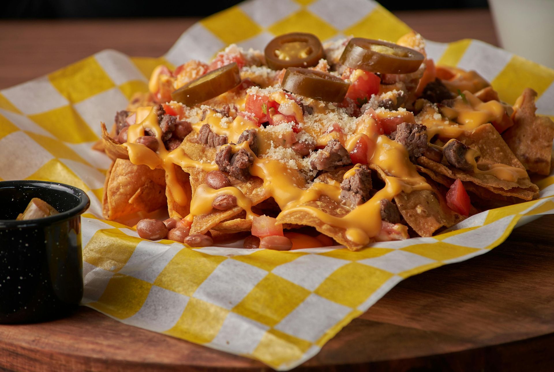 A close up of a plate of nachos on a checkered napkin on a table.