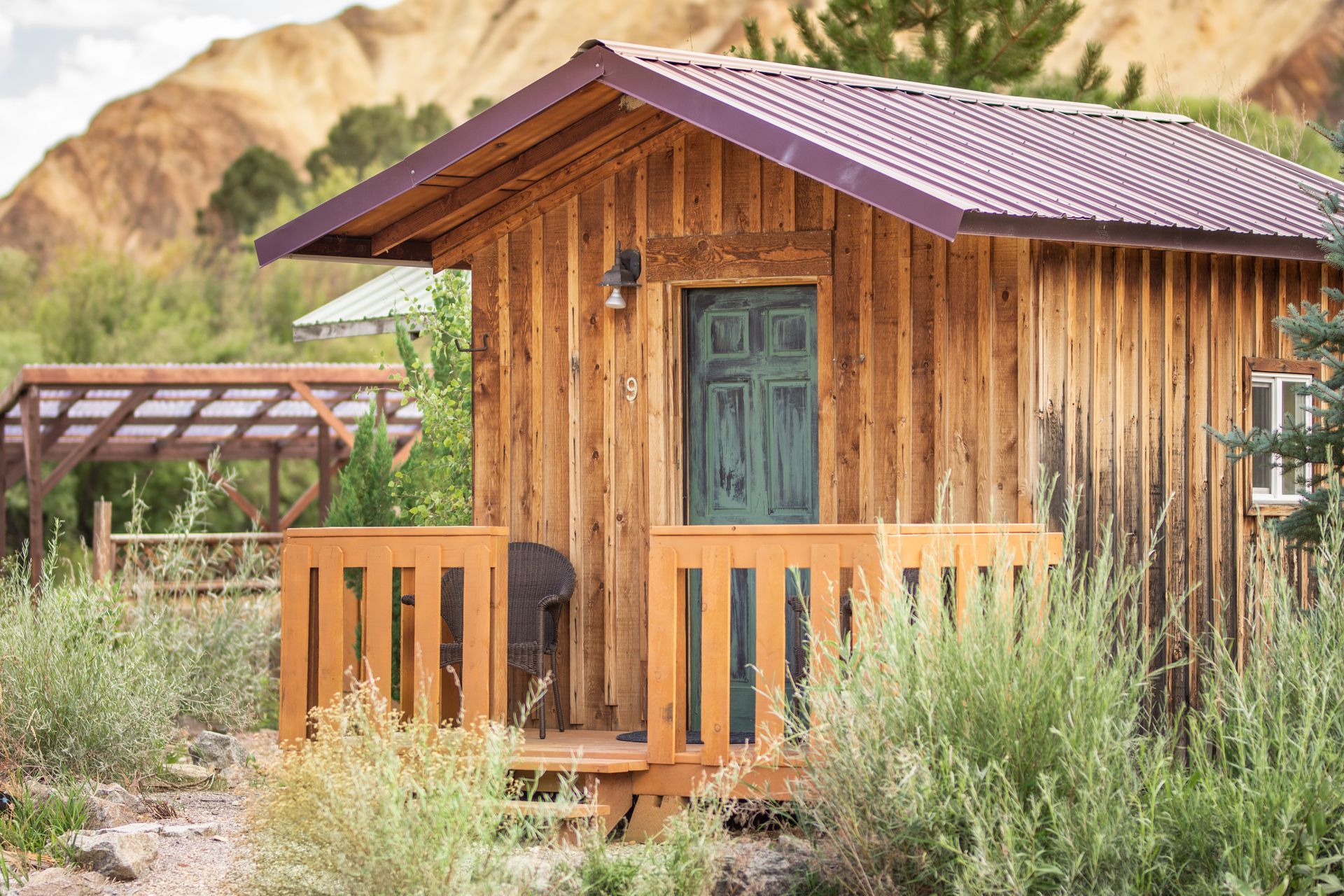 A small wooden cabin with a porch and mountains in the background.